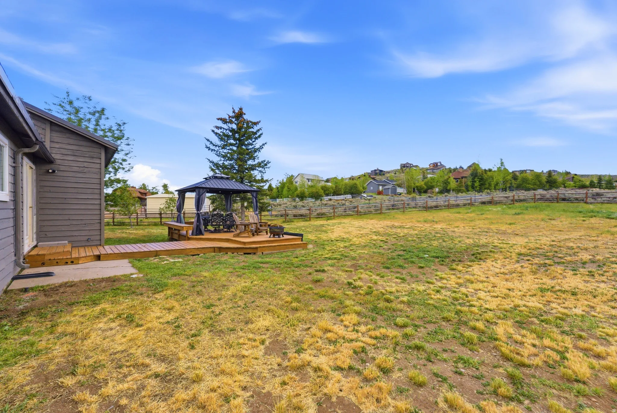 Expansive backyard featuring a multi-tiered wooden deck with a gazebo, a gravel patch, and a mature evergreen tree