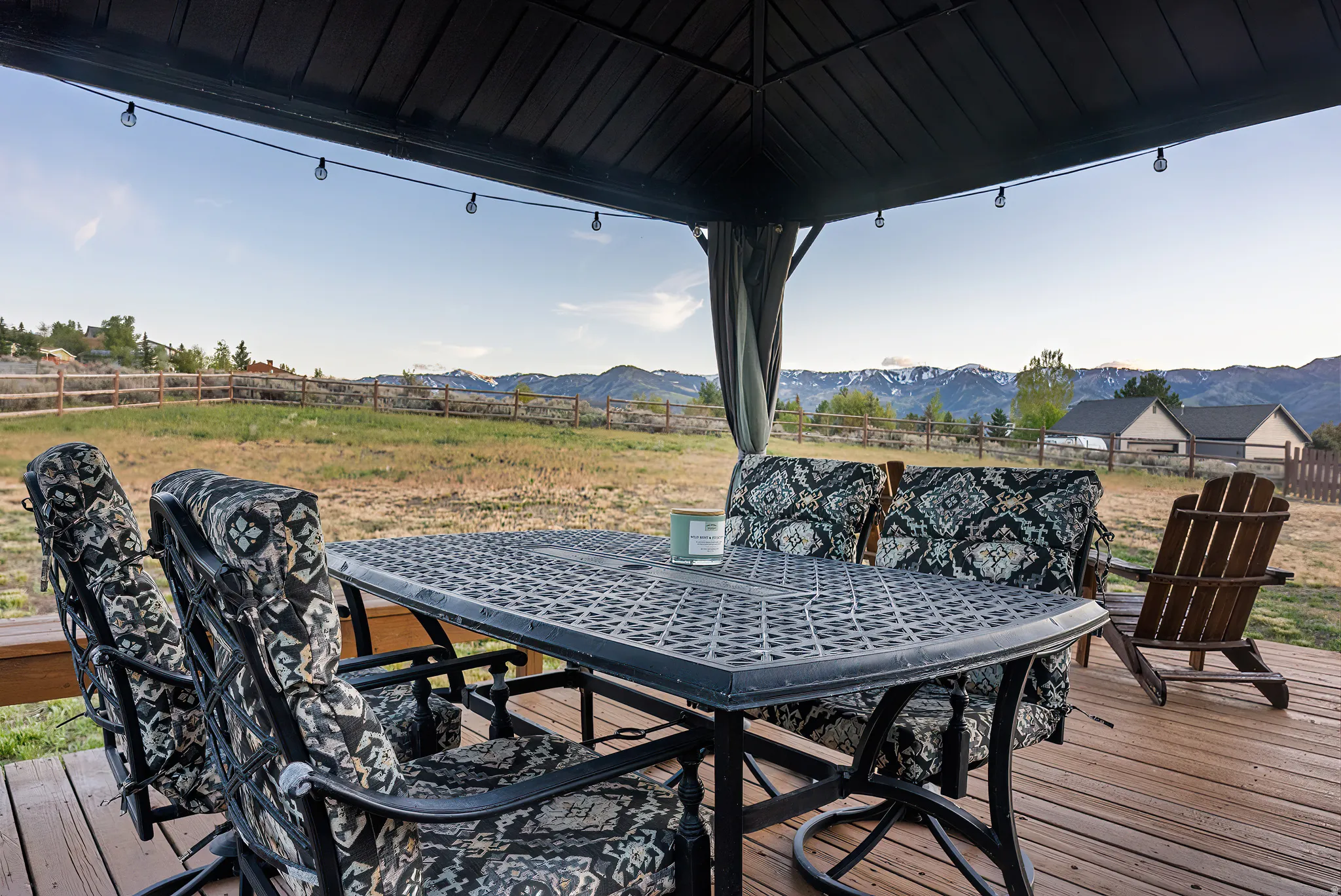 Covered outdoor deck with string lighting, overlooking a fenced expansive yard and distant mountains