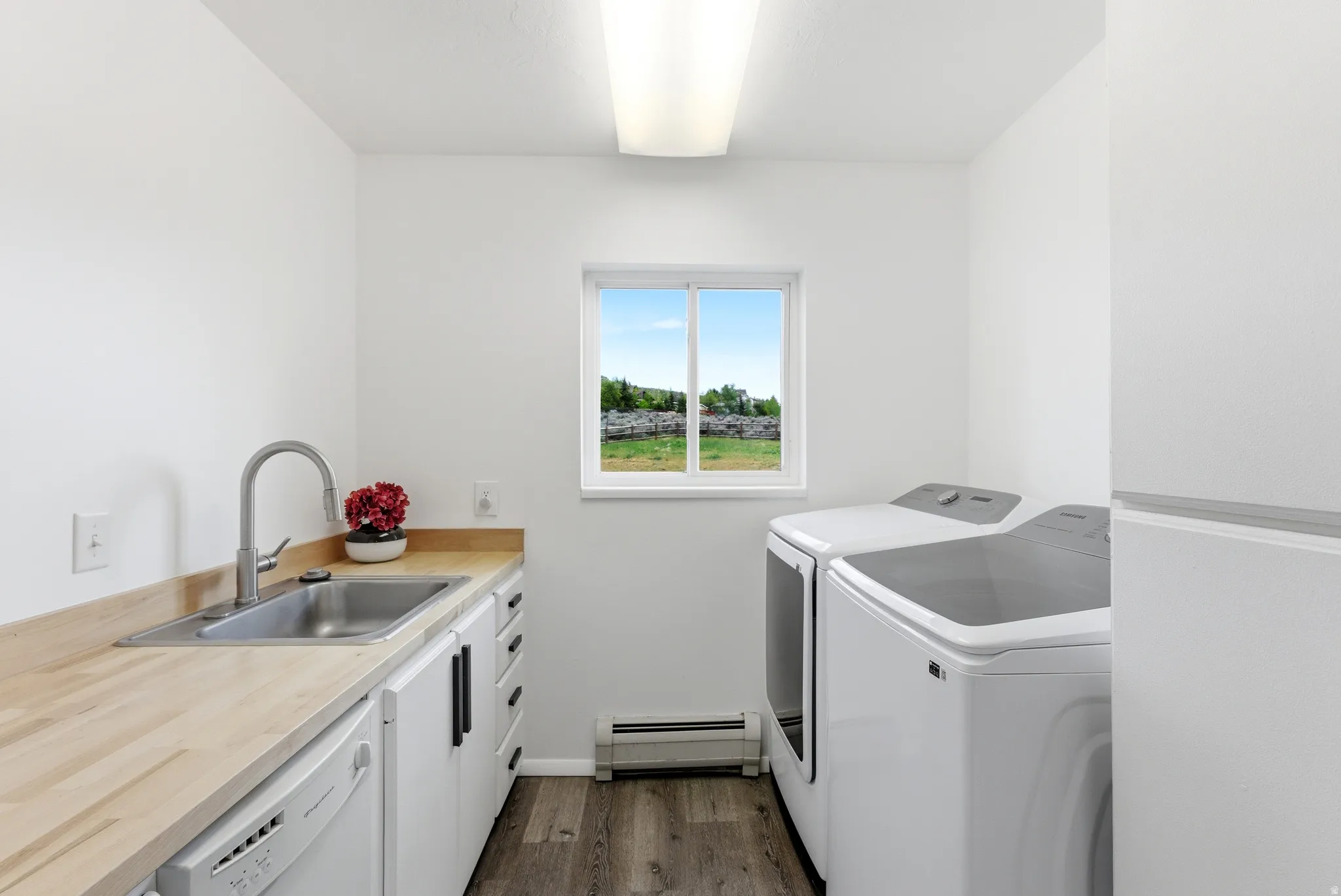 Laundry area featuring white cabinetry, a built-in stainless steel sink with a gooseneck faucet, light wood-finish countertops, and wood-finish flooring