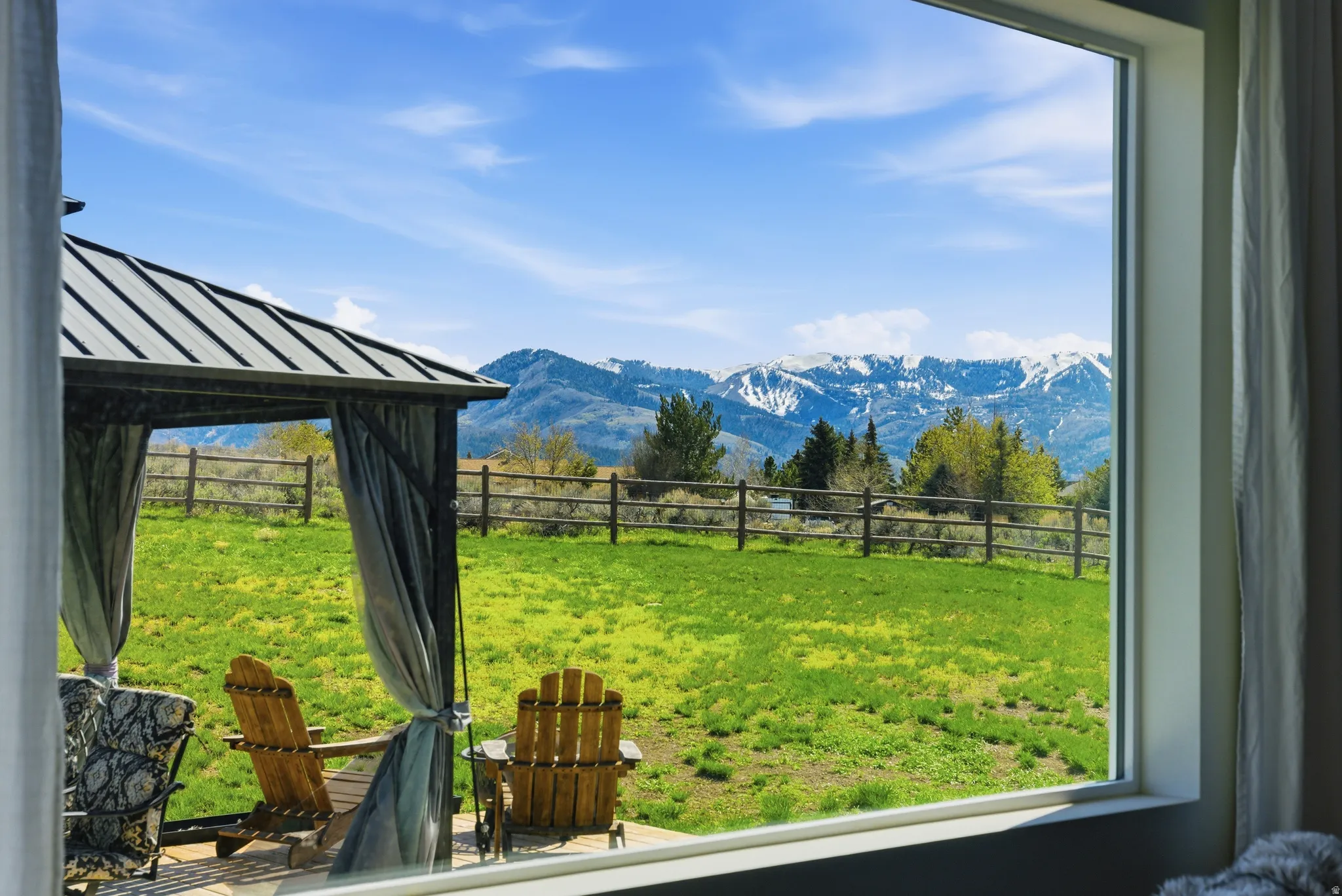 Expansive outdoor space featuring a covered gazebo with a metal roof, a wooden privacy fence, and a backdrop of distant snow-capped mountains