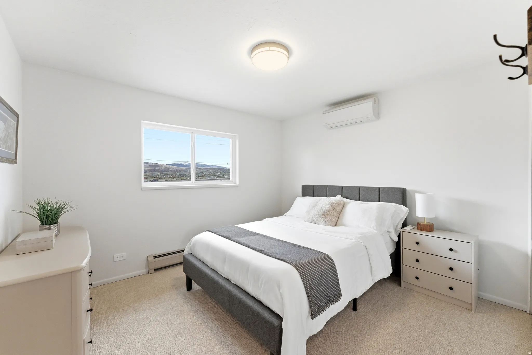 Bright bedroom featuring a large window, neutral carpeting, and a wall-mounted climate control unit