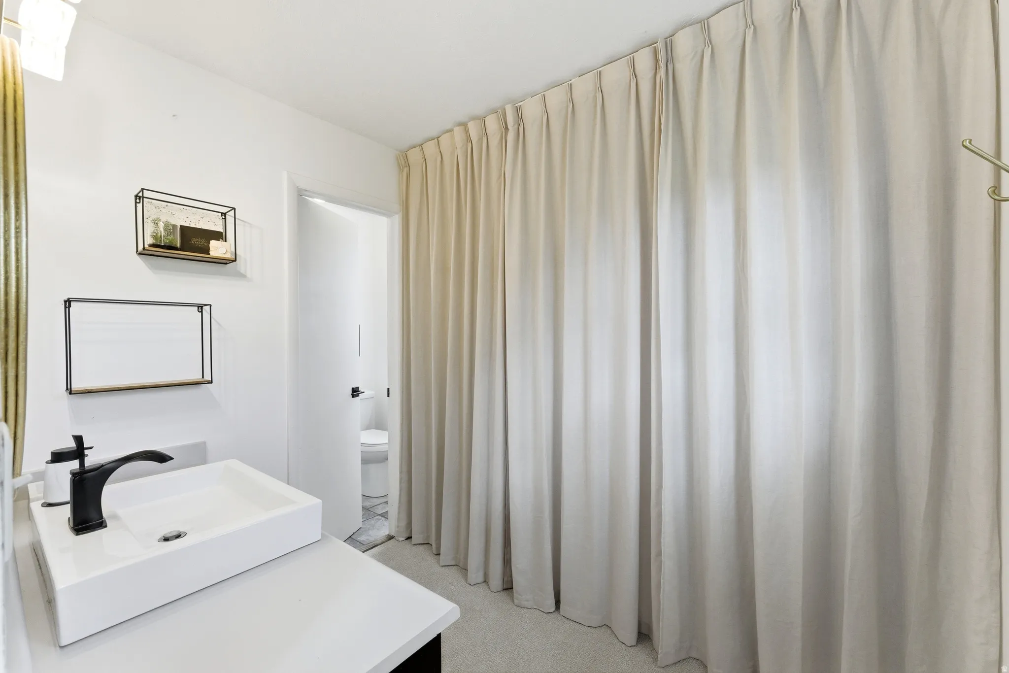 Bathroom featuring a rectangular vessel sink with a matte black faucet, light countertop, and full-height curtain enclosure