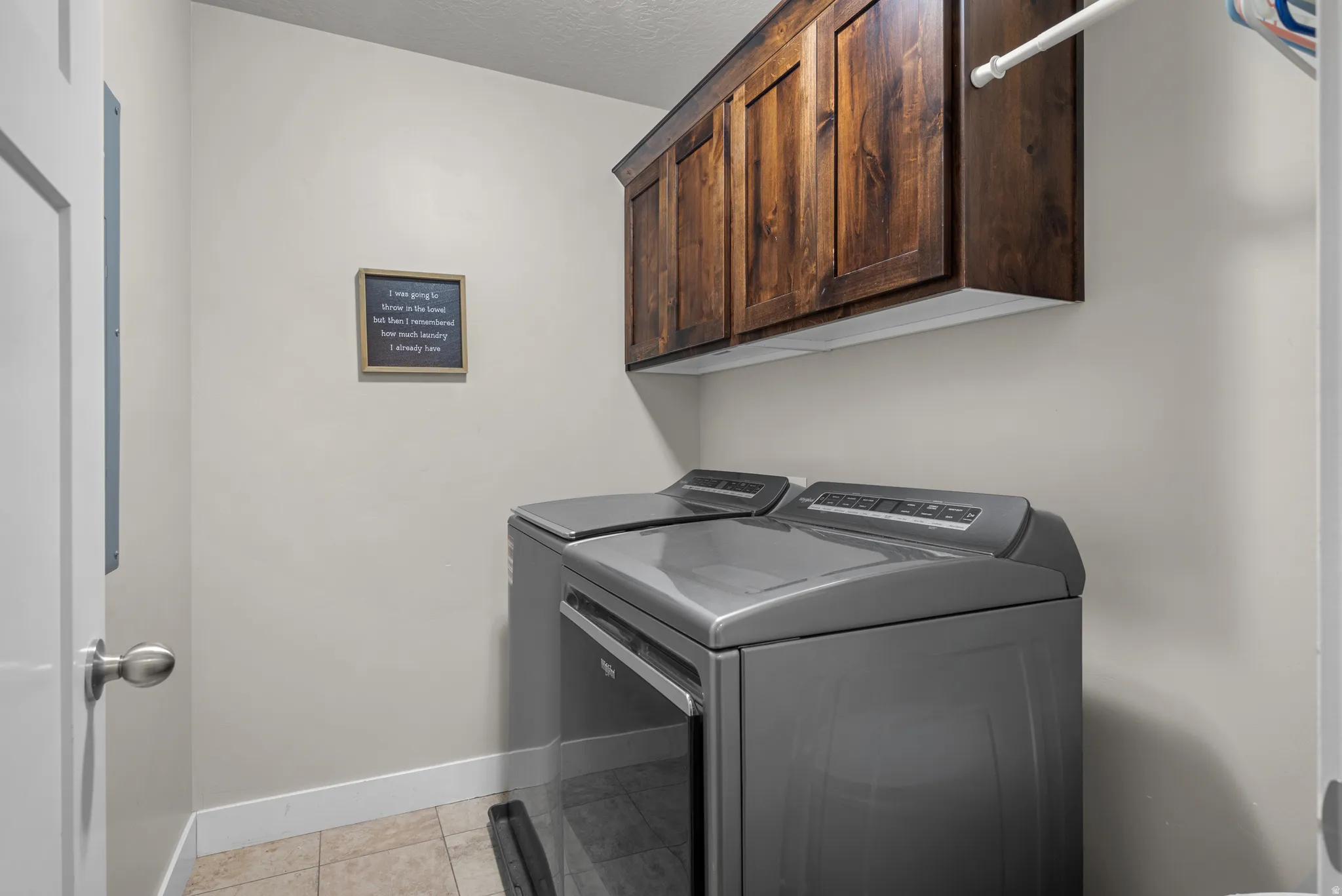 Laundry area featuring dark wood-finish cabinetry, a chrome hanging rod, and light-toned tile flooring