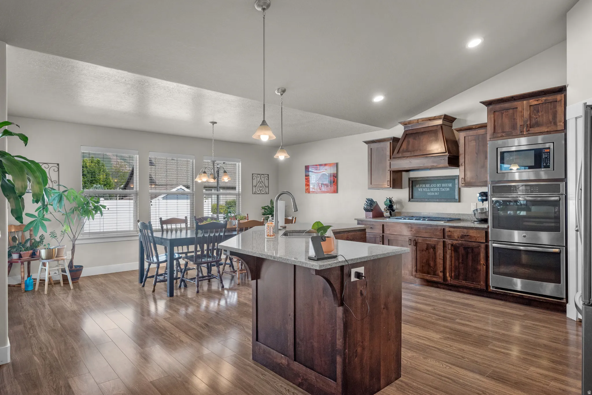 Spacious kitchen featuring a central island with a light-colored countertop, dark wood-finish cabinetry, stainless steel double ovens, and wood-finish flooring
