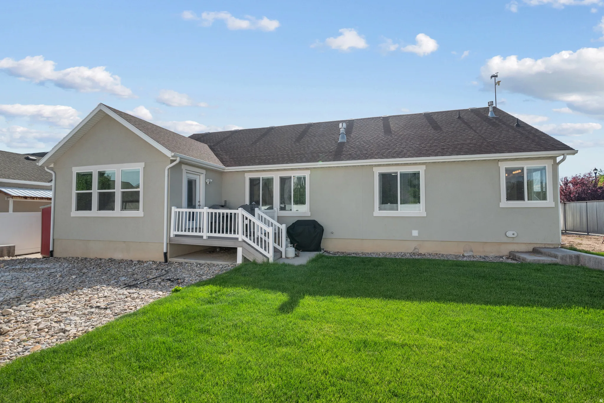 Rear exterior featuring a large green lawn, a white-railed deck with stairs, multiple windows with white trim, and a low-pitched roof