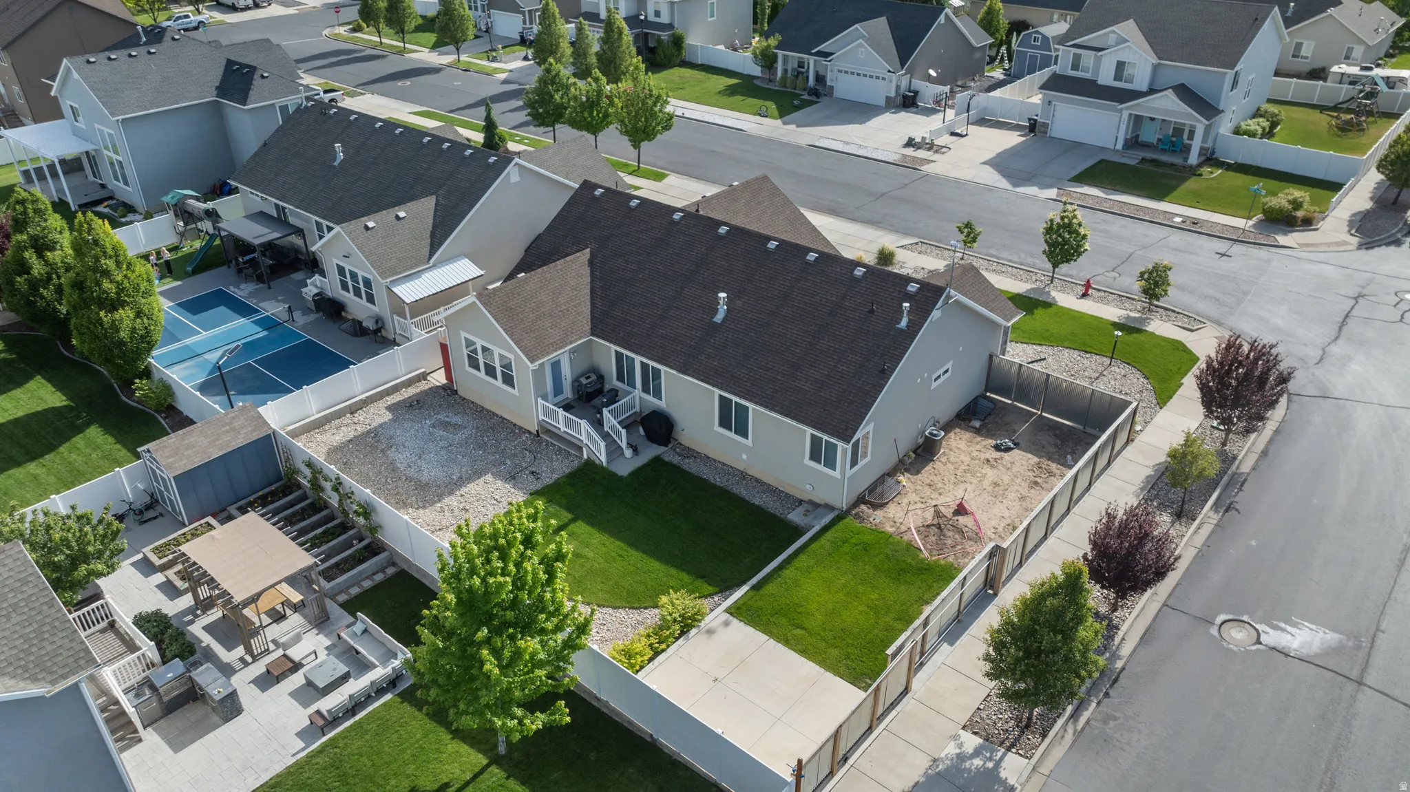 Rear exterior showcasing a manicured lawn, a concrete patio, a private fenced yard, mature landscaping, and a sport court