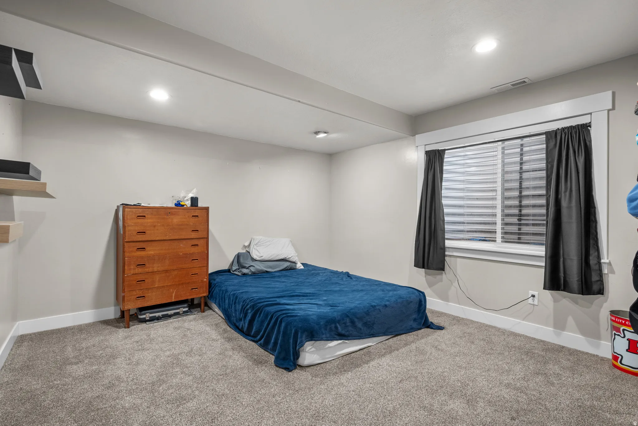 Carpeted room featuring a single window with blinds, recessed lighting, and wall-mounted shelving