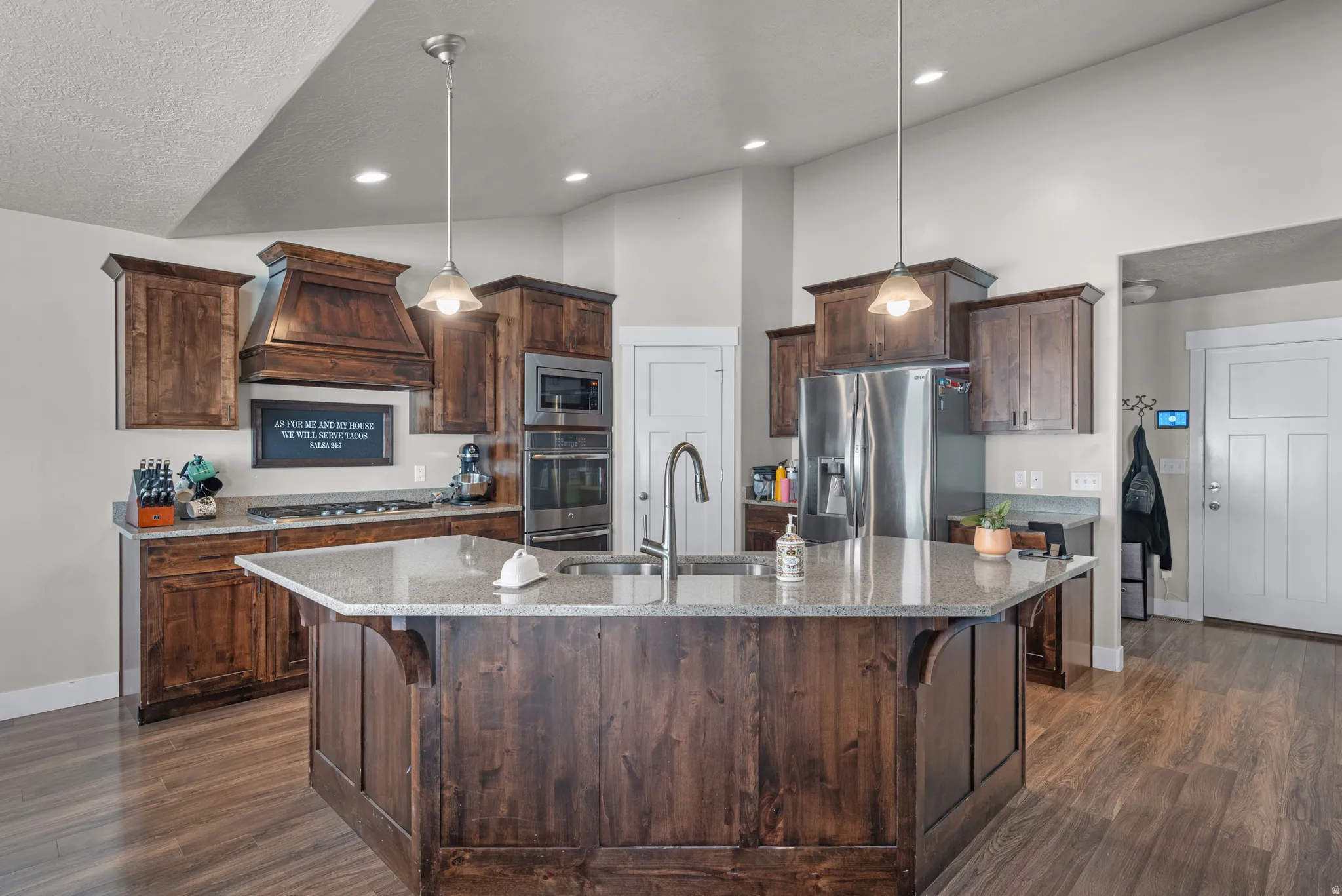 Expansive kitchen featuring a large central island with a sink, wood-finish cabinetry, stainless steel appliances, granite countertops, and wood-finish flooring