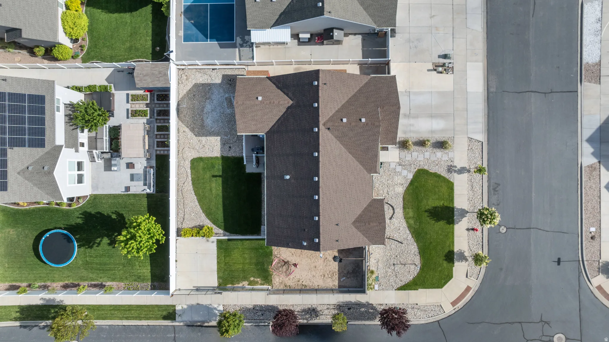 Overhead perspective showcasing a residential property with a dark shingle roof, concrete driveway, and front lawn