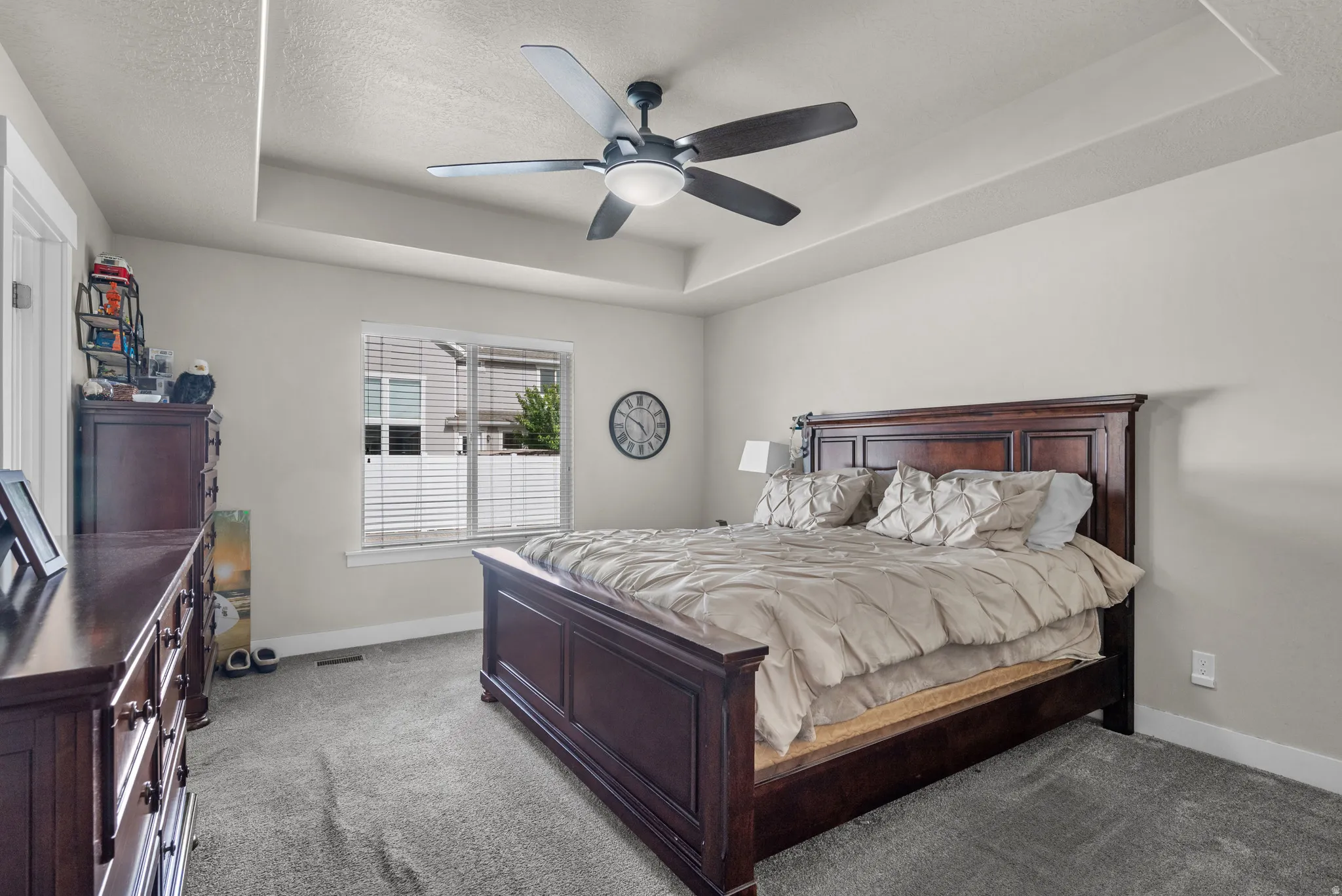 Spacious bedroom featuring a recessed ceiling, gray carpeting, a large window with blinds, and a ceiling fan with integrated lighting