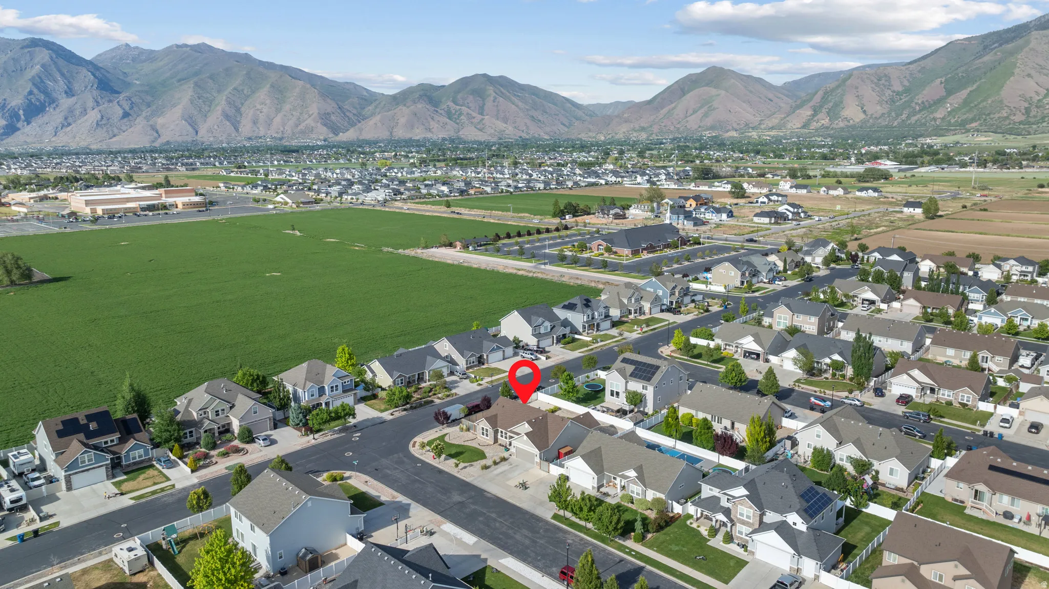 Aerial view showcasing a residential neighborhood with mountain backdrops and a prominent green field bordering the community