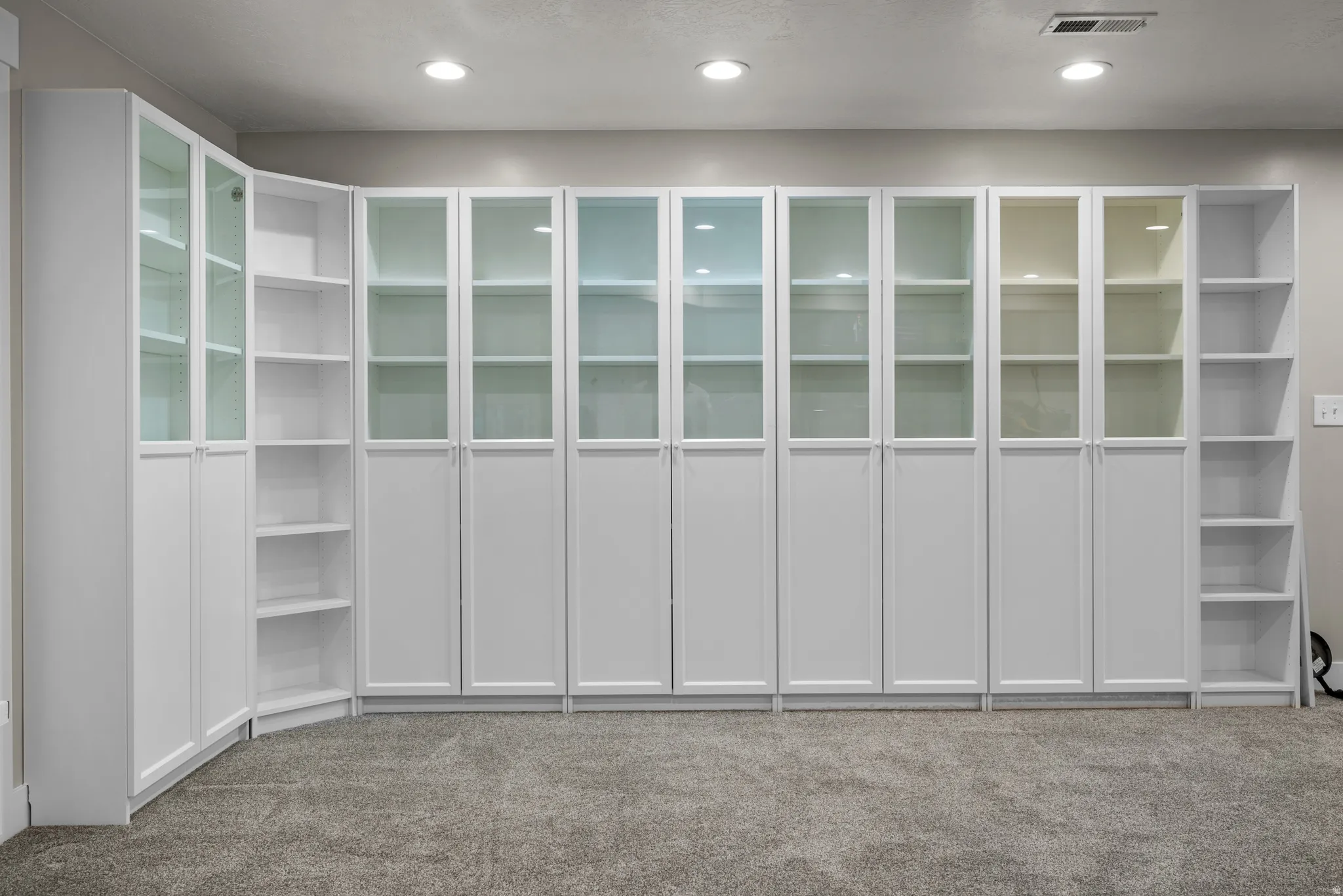 Extensive built-in storage system featuring white cabinetry, glass-front upper doors, open shelving, and a corner configuration