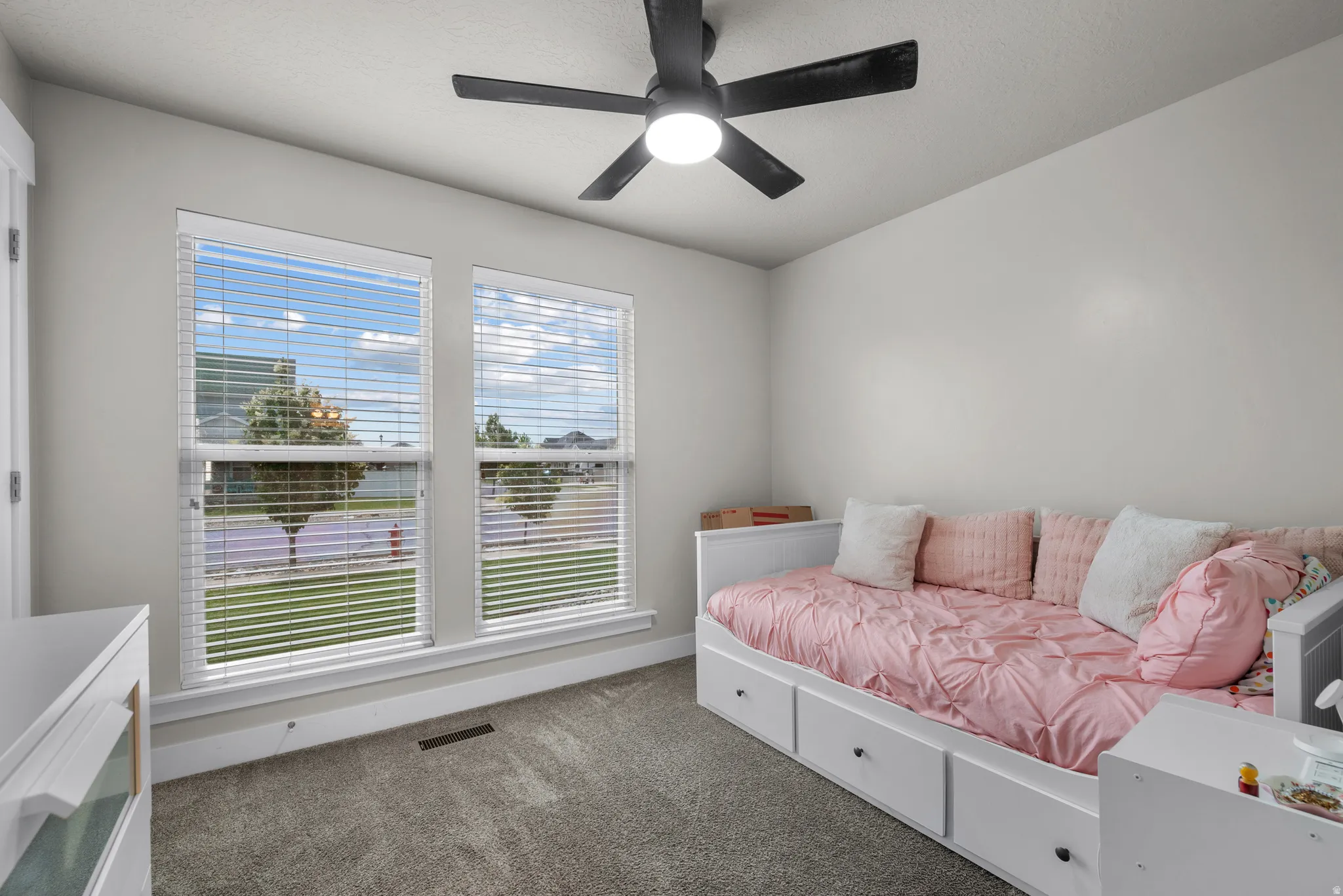 Carpeted room featuring a ceiling fan with integrated lighting, two double-hung windows with blinds, and white baseboards