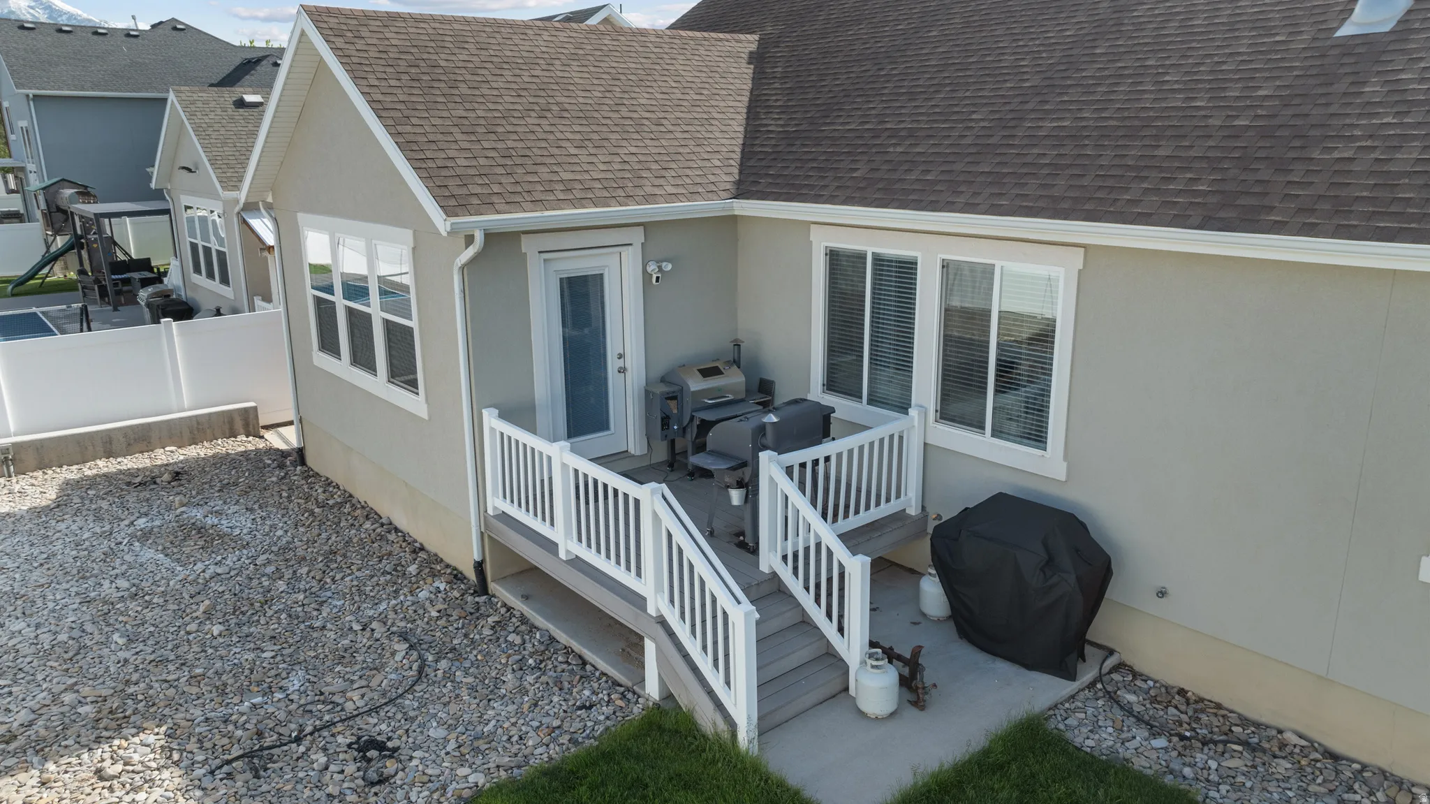 Rear exterior featuring a multi-level deck with white railings, a tan stucco finish, and multiple windows