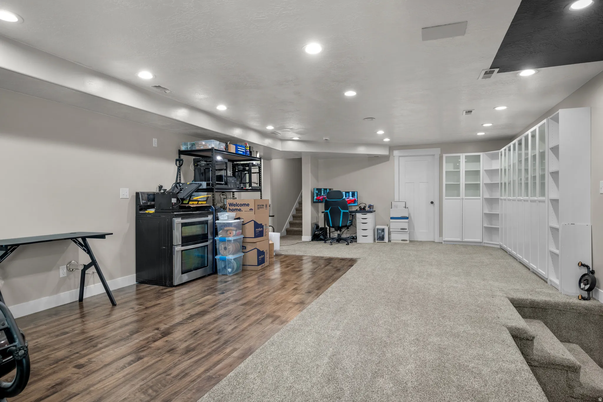 Spacious lower level featuring recessed lighting, a combination of wood-finish flooring and carpet, and extensive built-in white cabinetry with glass-front storage