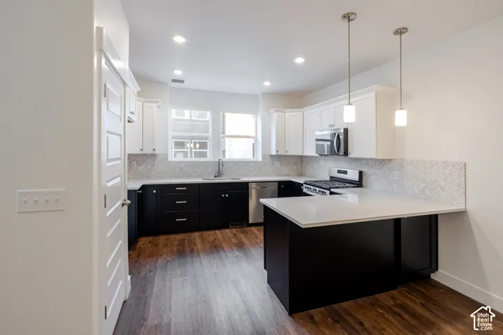 Kitchen featuring wood-finish flooring, two-tone cabinetry, stainless steel appliances, white countertops, and a herringbone tile backsplash