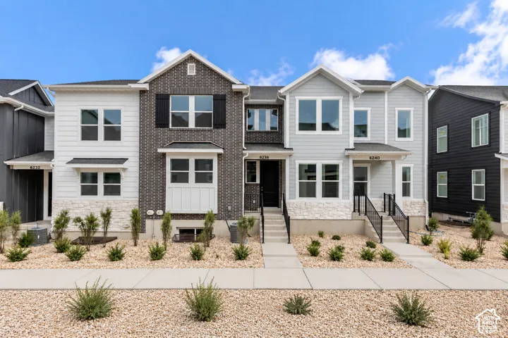 Two-story townhouse featuring a brick and siding exterior, white stone accents, an elevated entry with black railings, and a low-maintenance gravel landscape