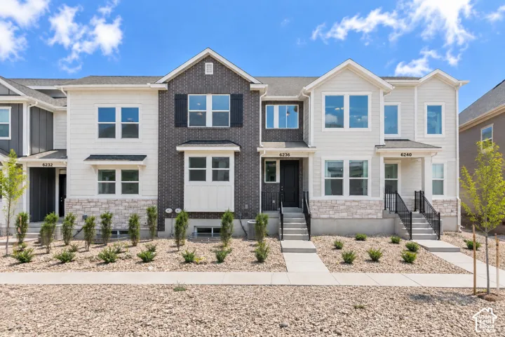 Multi-story townhome exterior featuring light-colored siding, dark brick accents, and stone detailing