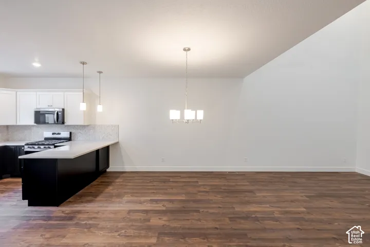 Wood-finish flooring, vaulted ceiling, white cabinetry, black base cabinetry, and a gas range