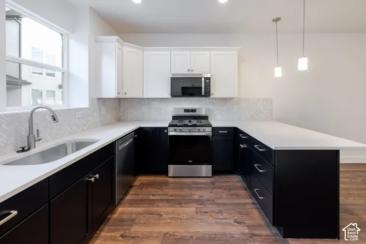U-shaped kitchen featuring wood-finish flooring, white countertops, stainless steel appliances, a herringbone tile backsplash, and two-tone cabinetry