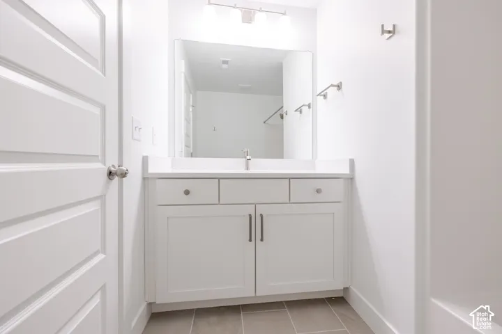 White vanity with integrated sink, white countertop, rectangular mirror, and tiled flooring