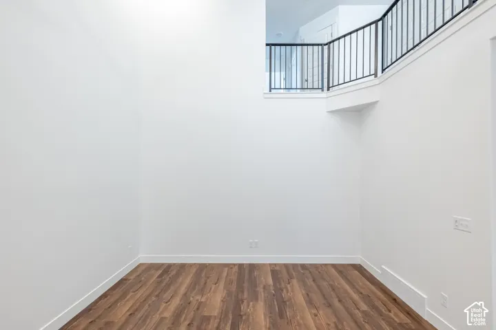 High ceilings in a room with wood-finish flooring, white walls, and a black metal railing on an upper level