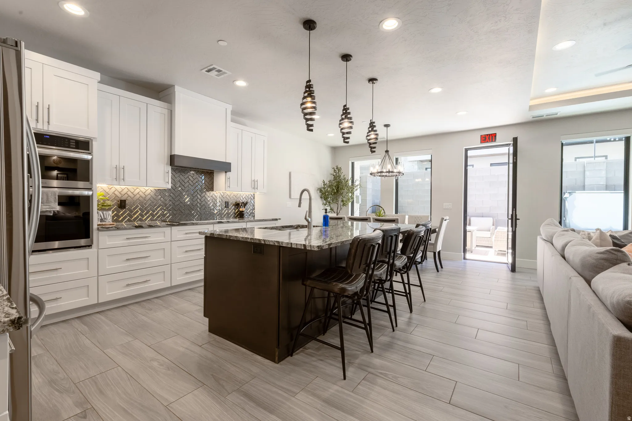Open-concept kitchen with crisp white cabinetry, built-in stainless steel appliances, a dark wood-finish island with a light-tone countertop, and a herringbone pattern tile backsplash