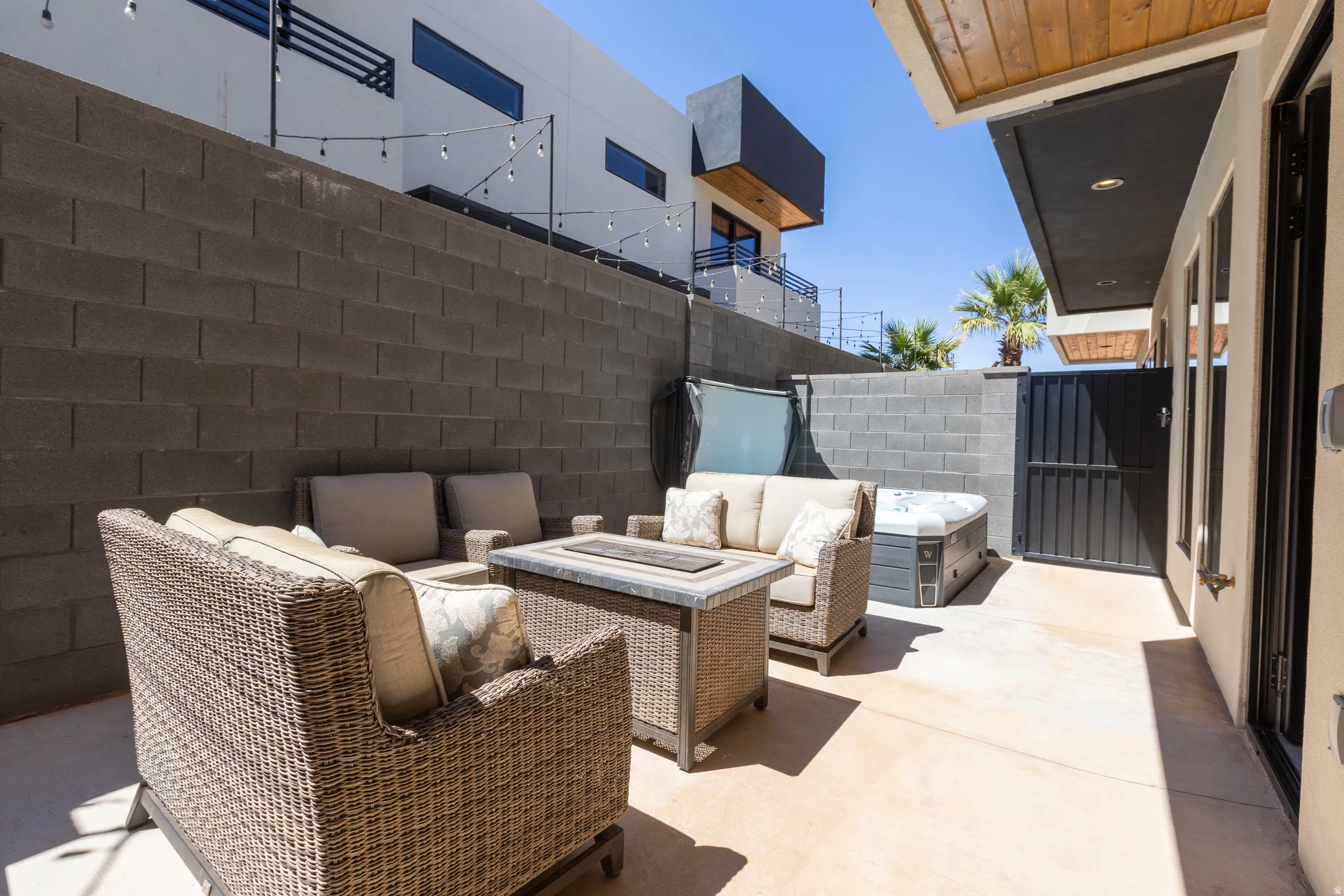 Paved outdoor patio featuring a privacy wall, a spa, and string lighting