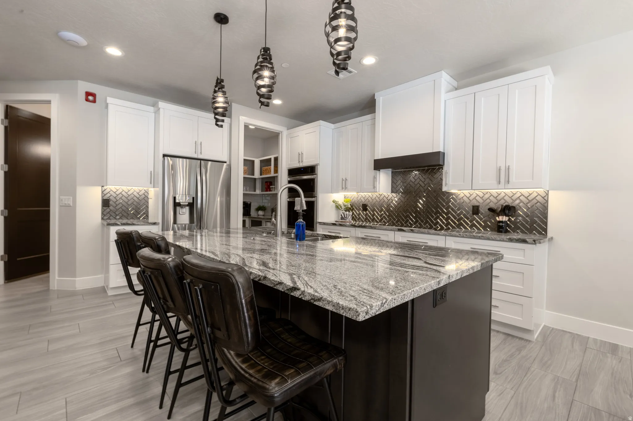 Kitchen featuring an oversized island with a stone countertop, white cabinetry, integrated stainless steel appliances, and a herringbone-patterned backsplash