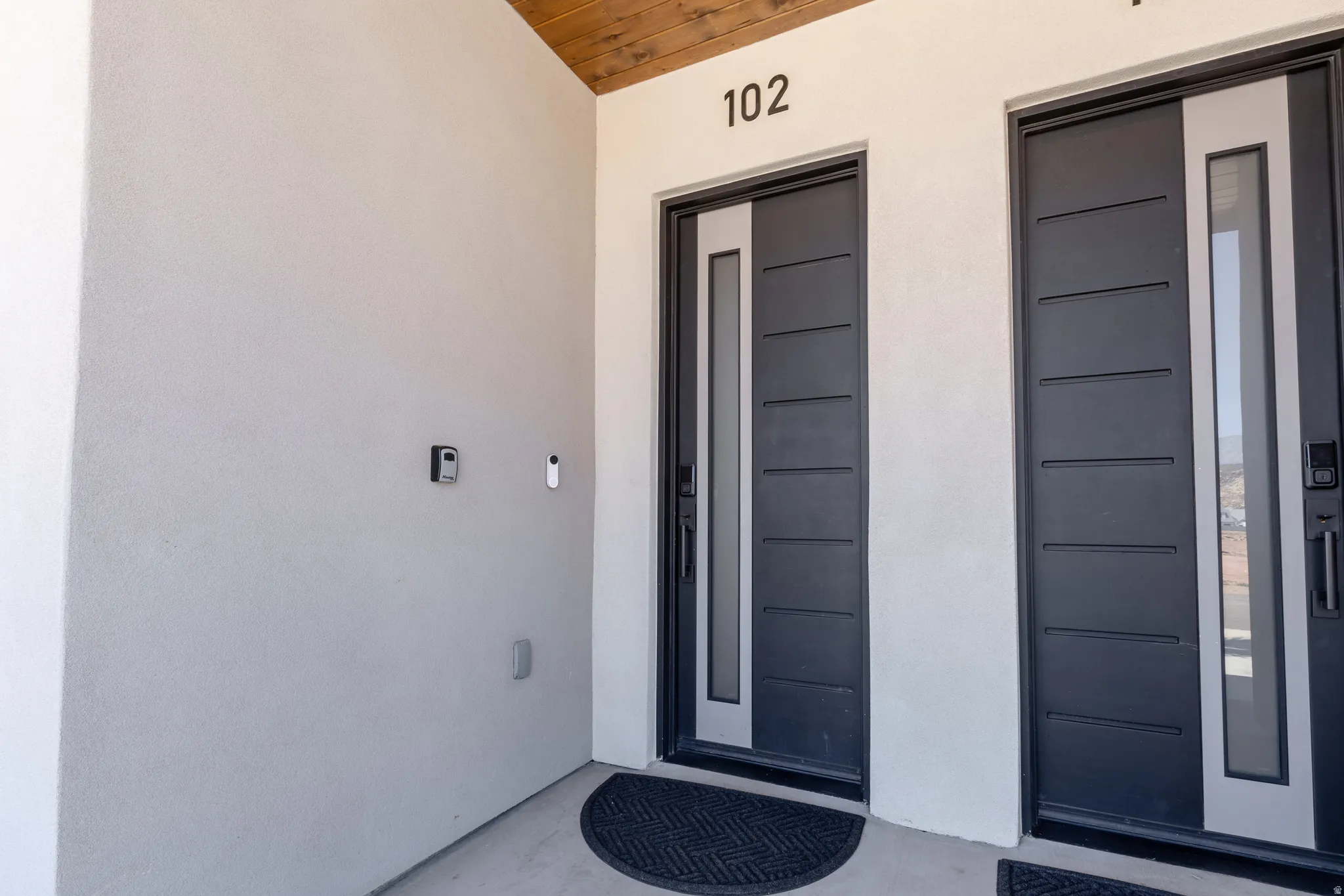 Modern entry featuring a dark gray door with horizontal paneling and a vertical frosted glass insert, complemented by a light-colored stucco exterior
