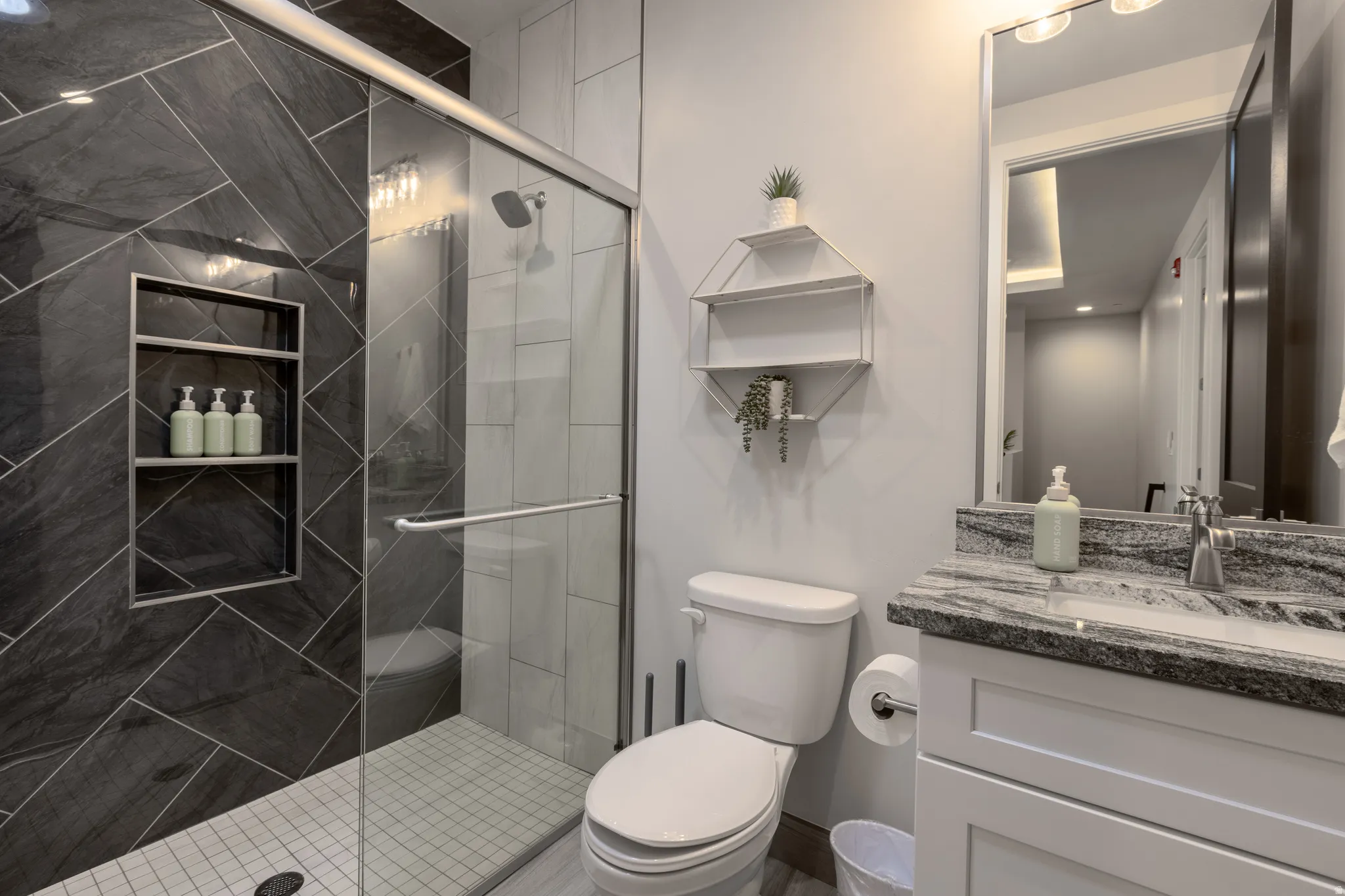 Shower with dark gray chevron-patterned wall tile, glass enclosure, and recessed shelving
