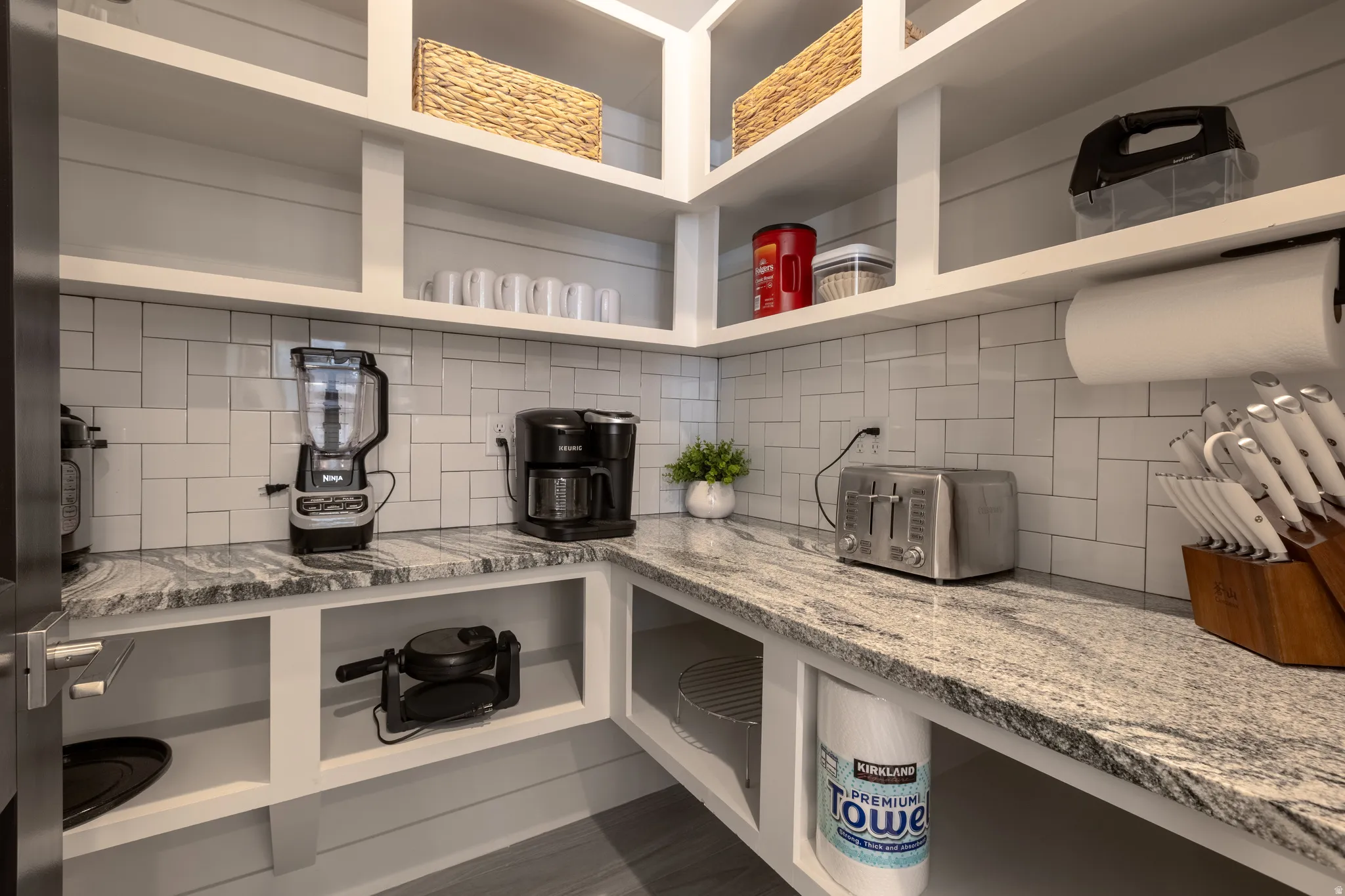 Walk-in pantry featuring white shaker-style shelving, white subway tile backsplash, and granite-style countertops