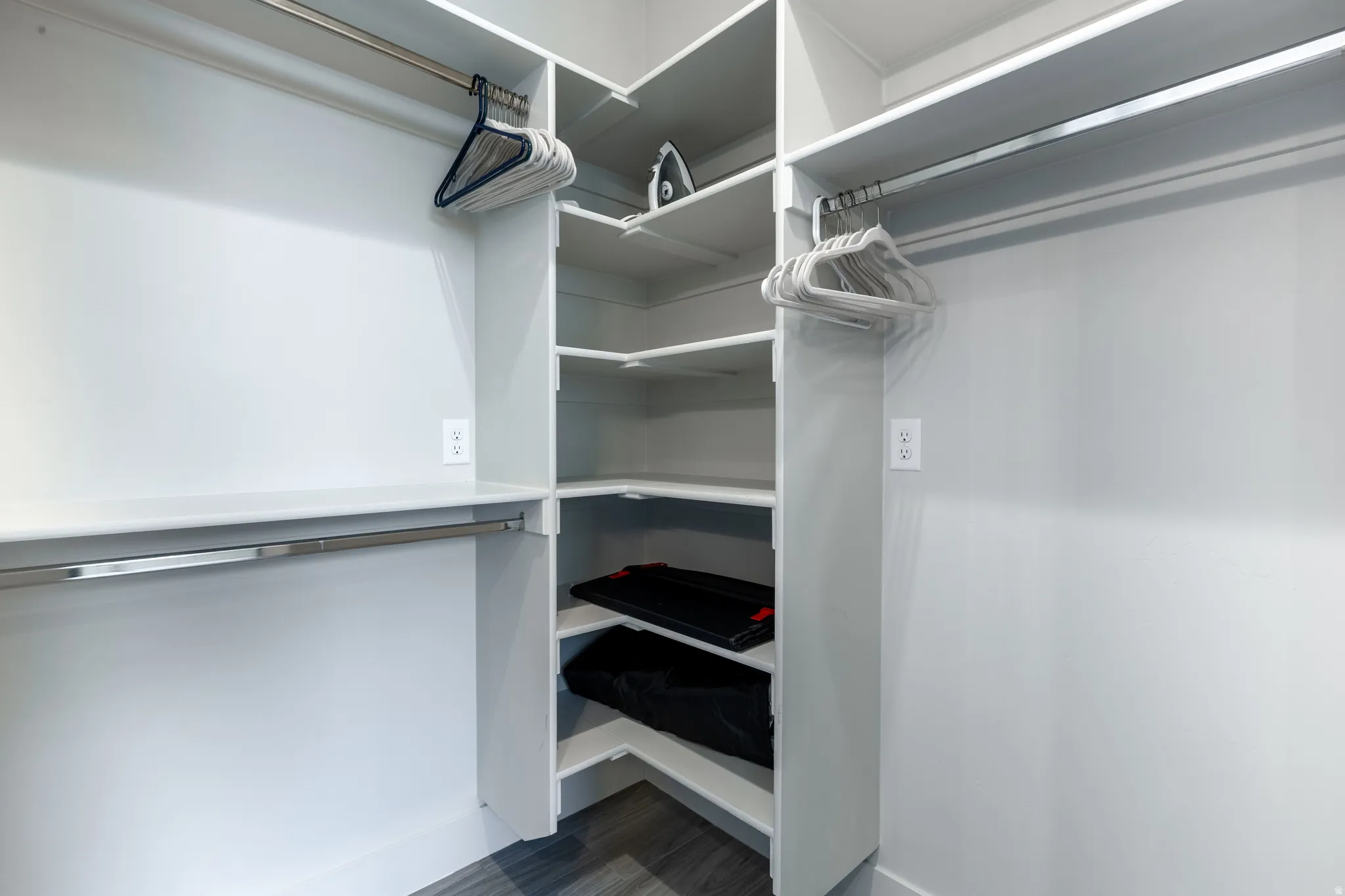 Custom closet system featuring multiple hanging rods, corner shelving units, and wood-finish flooring