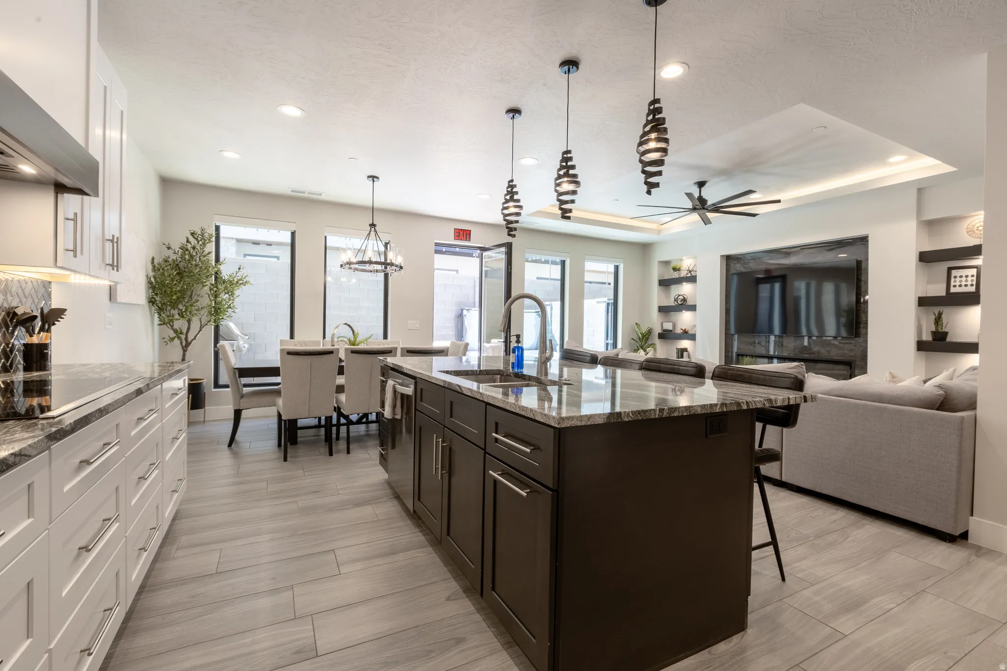 Spacious open-concept kitchen featuring a large island with a sink, white cabinetry with dark countertops, wood-finish flooring, recessed lighting, and a dining area with ample window light