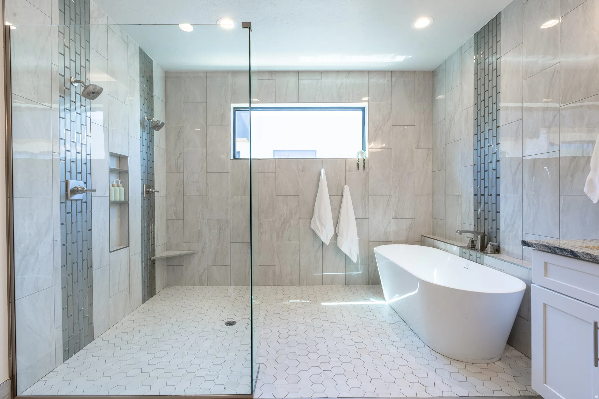 Spacious bathroom featuring a frameless glass shower enclosure, a freestanding soaking tub, and hexagon tile flooring