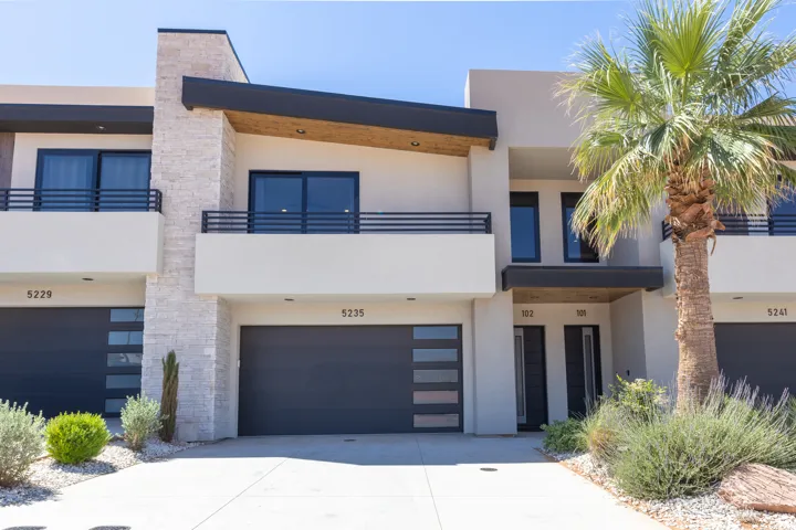 Contemporary stucco exterior featuring a stone accent column, dark-framed windows, and metal balcony railings