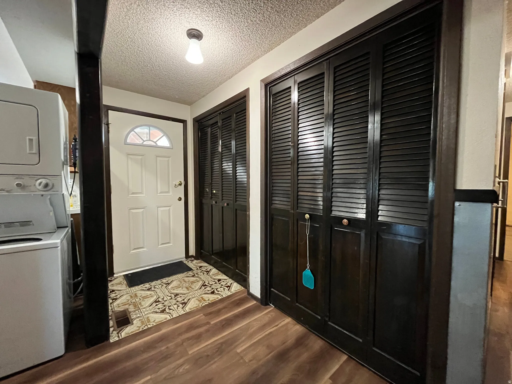 Entryway featuring wood-finish flooring, a white paneled door with an arched window, and dark louvered bifold doors