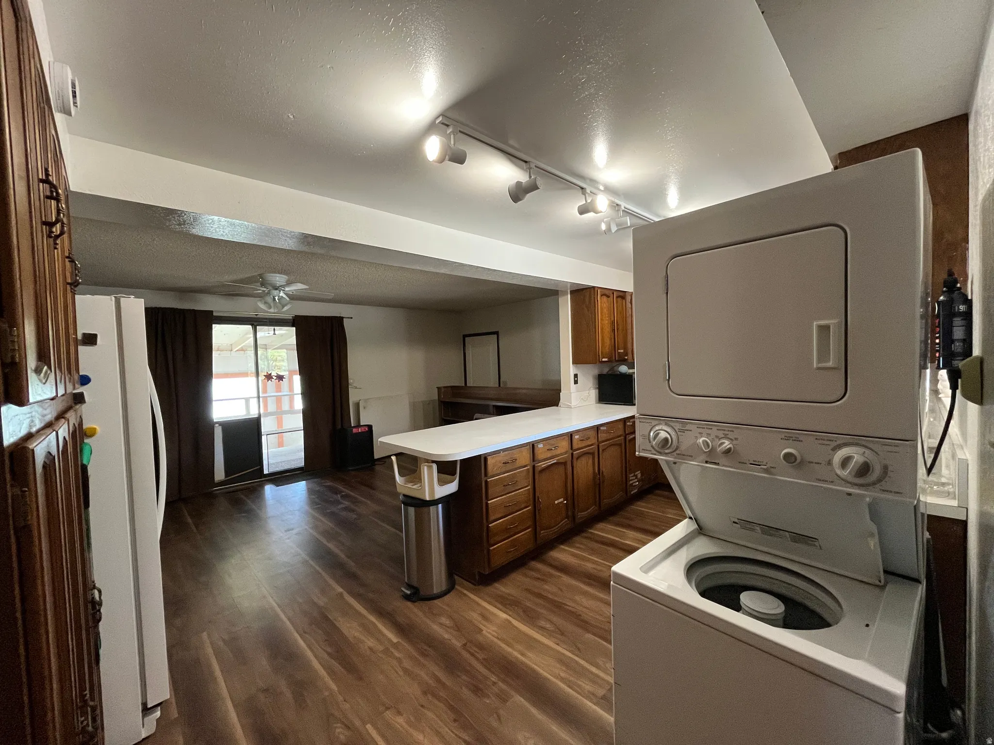 Open-concept living space featuring wood-finish flooring, a full kitchen with wood cabinetry and track lighting, and a sliding glass door leading to an outdoor deck