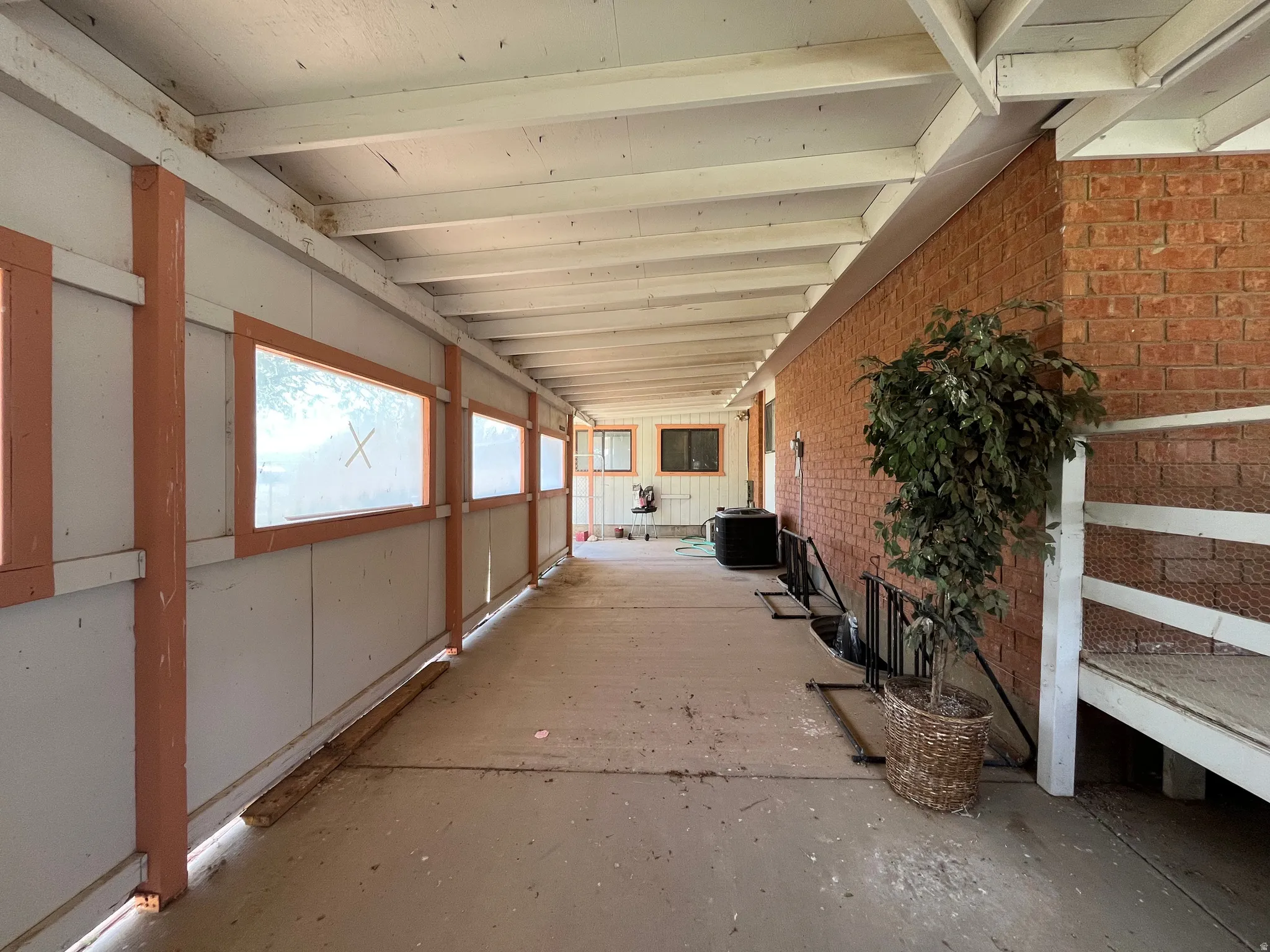 Covered outdoor corridor featuring a concrete floor, exposed wood beam ceiling, and a brick exterior wall