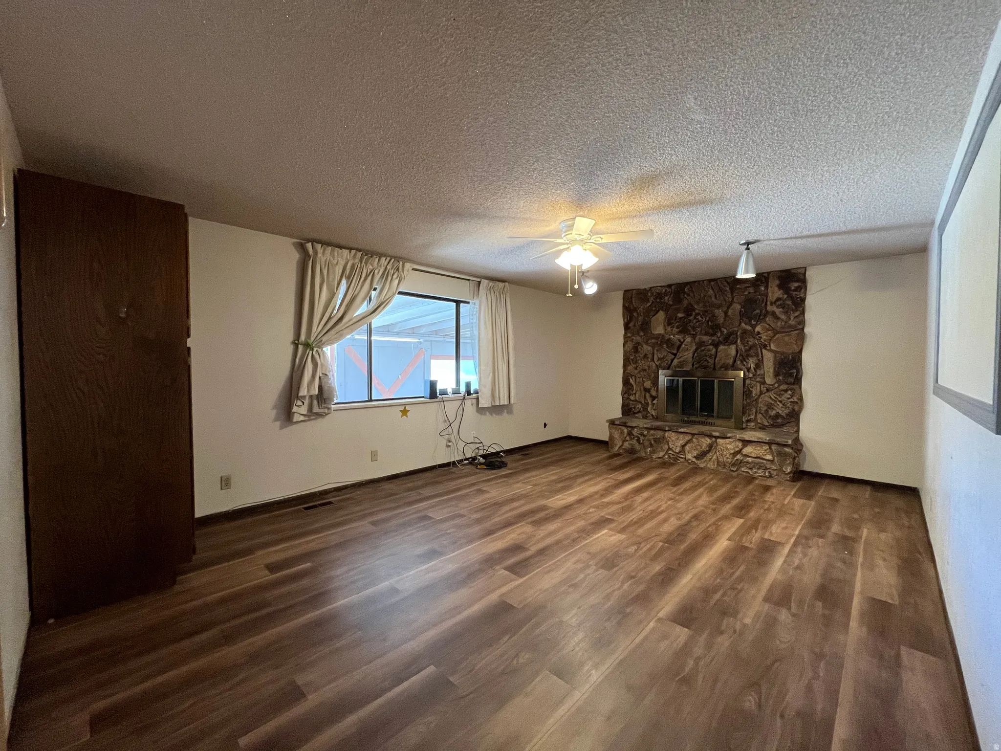 Spacious room featuring wood-finish flooring, a stone fireplace with a metal insert, and a ceiling fan with integrated lighting