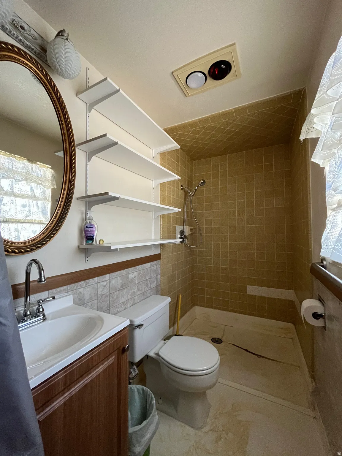 Bathroom featuring a wood-finish vanity with an integrated sink, a large oval mirror, and wall-mounted shelving