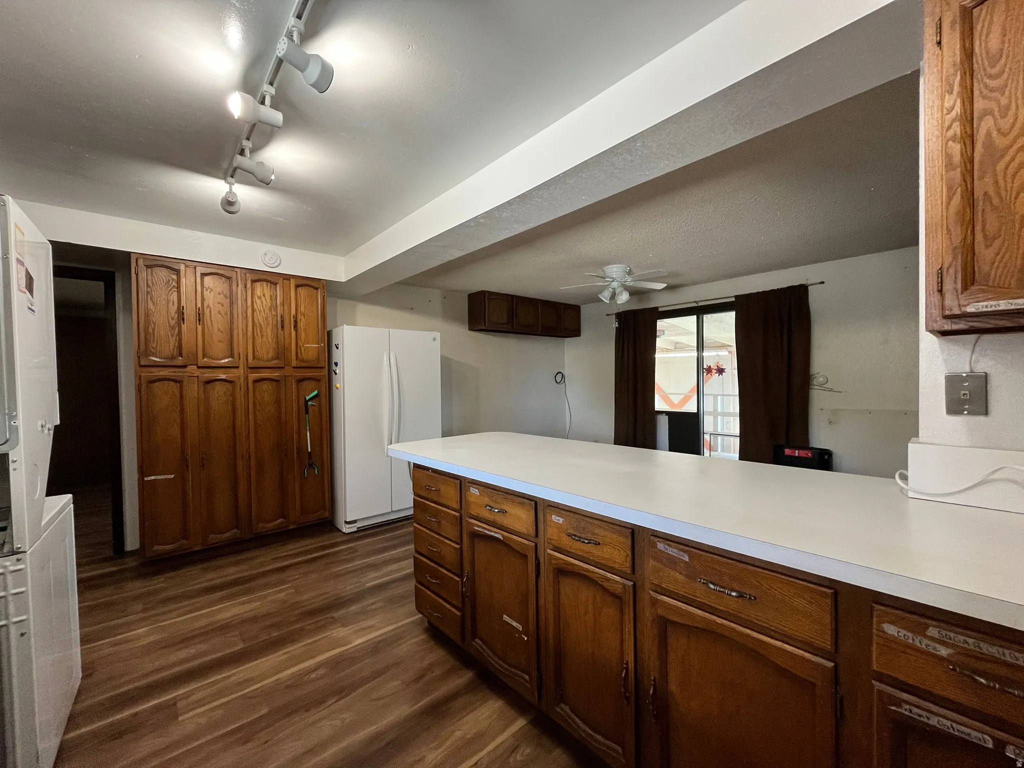 Kitchen featuring extensive wood cabinetry, white countertops, wood-finish flooring, track lighting, and a ceiling fan