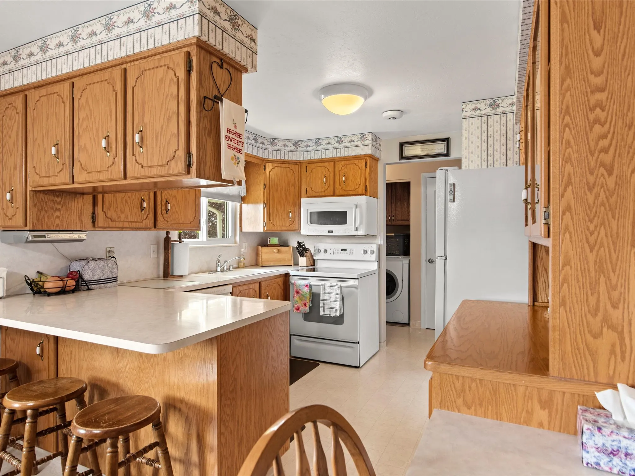 Kitchen featuring light wood cabinetry, white countertops, built-in microwave, white appliances, and a window above the sink