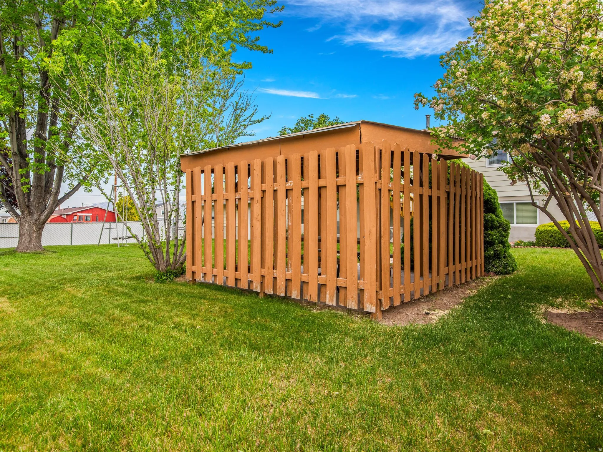 Enclosed utility area featuring a wooden fence with vertical slats, surrounded by a manicured lawn and mature trees