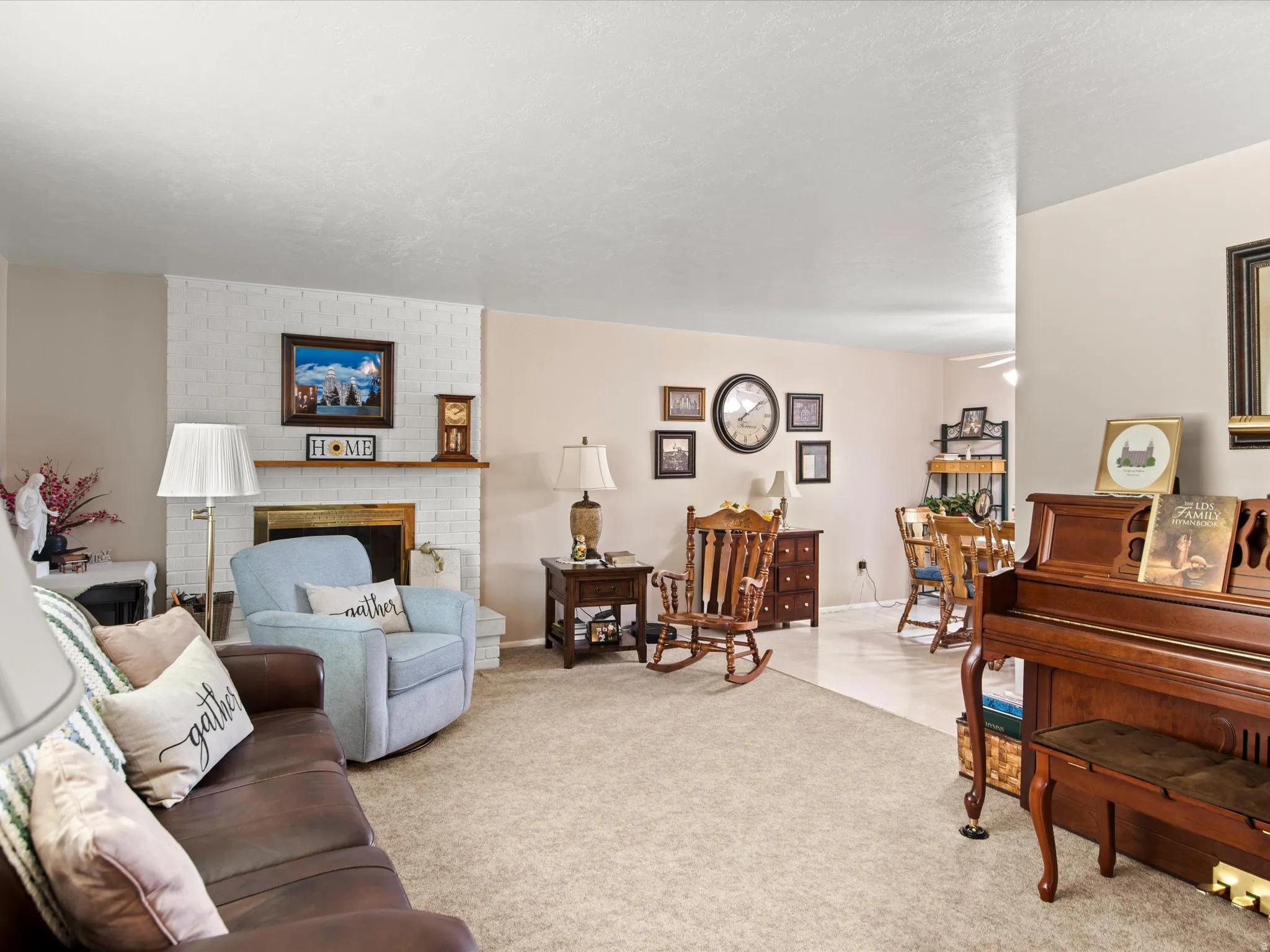 Living area featuring a white brick fireplace with a wood mantle, carpeted flooring, and light-toned walls