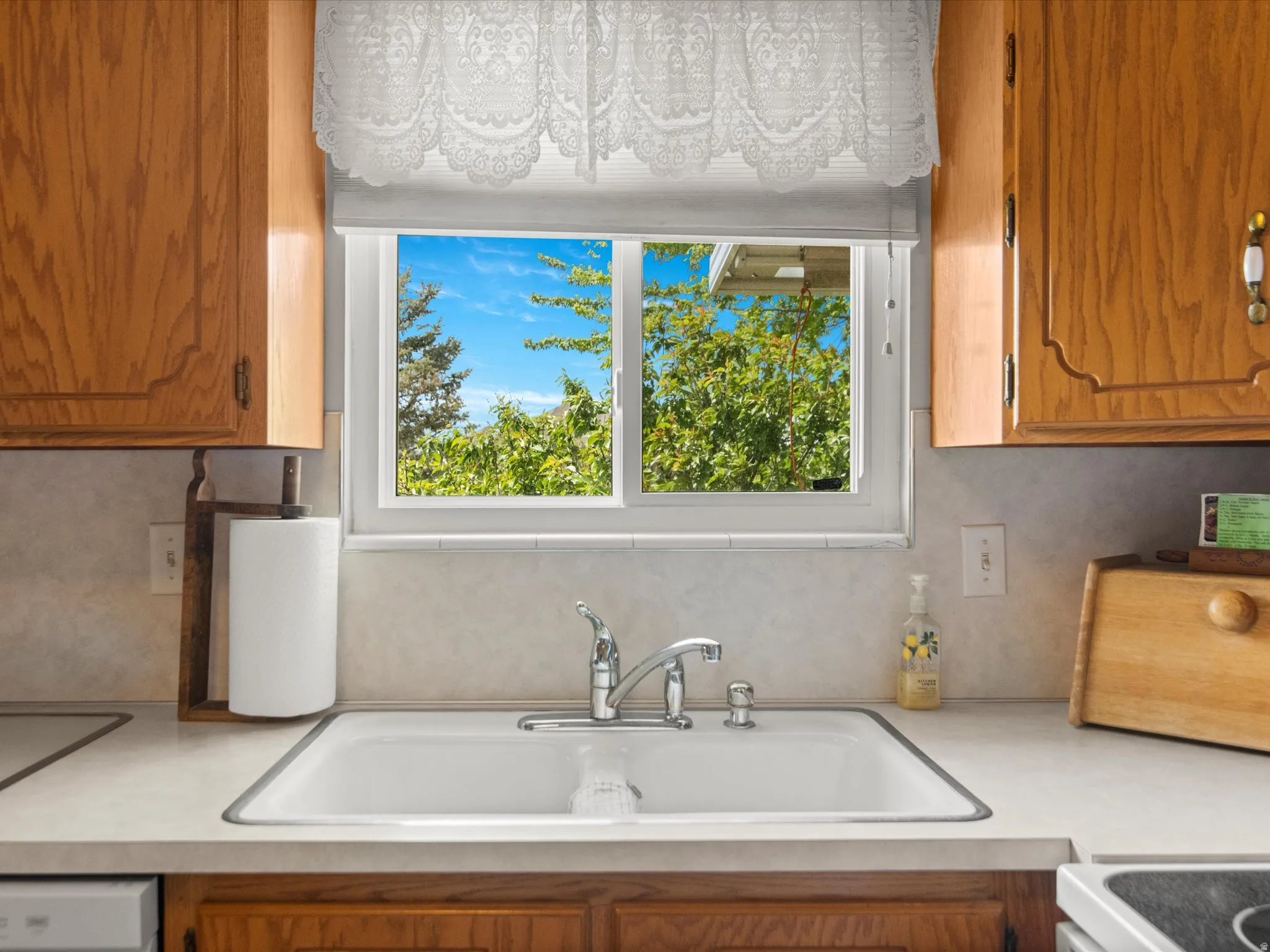 White kitchen sink with chrome faucet, set within light countertops and oak cabinetry