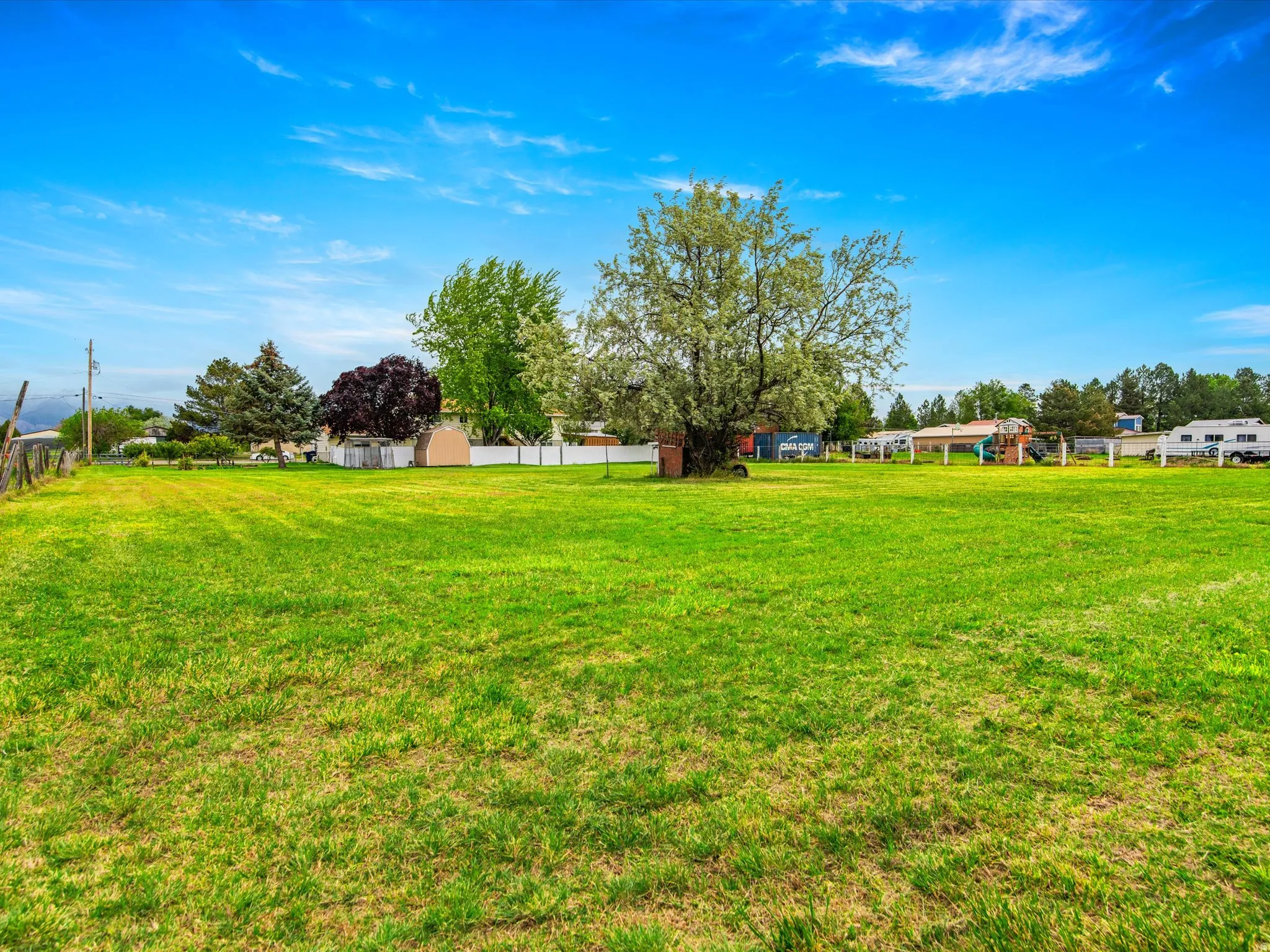 Expansive green lawn with mature trees and a perimeter fence