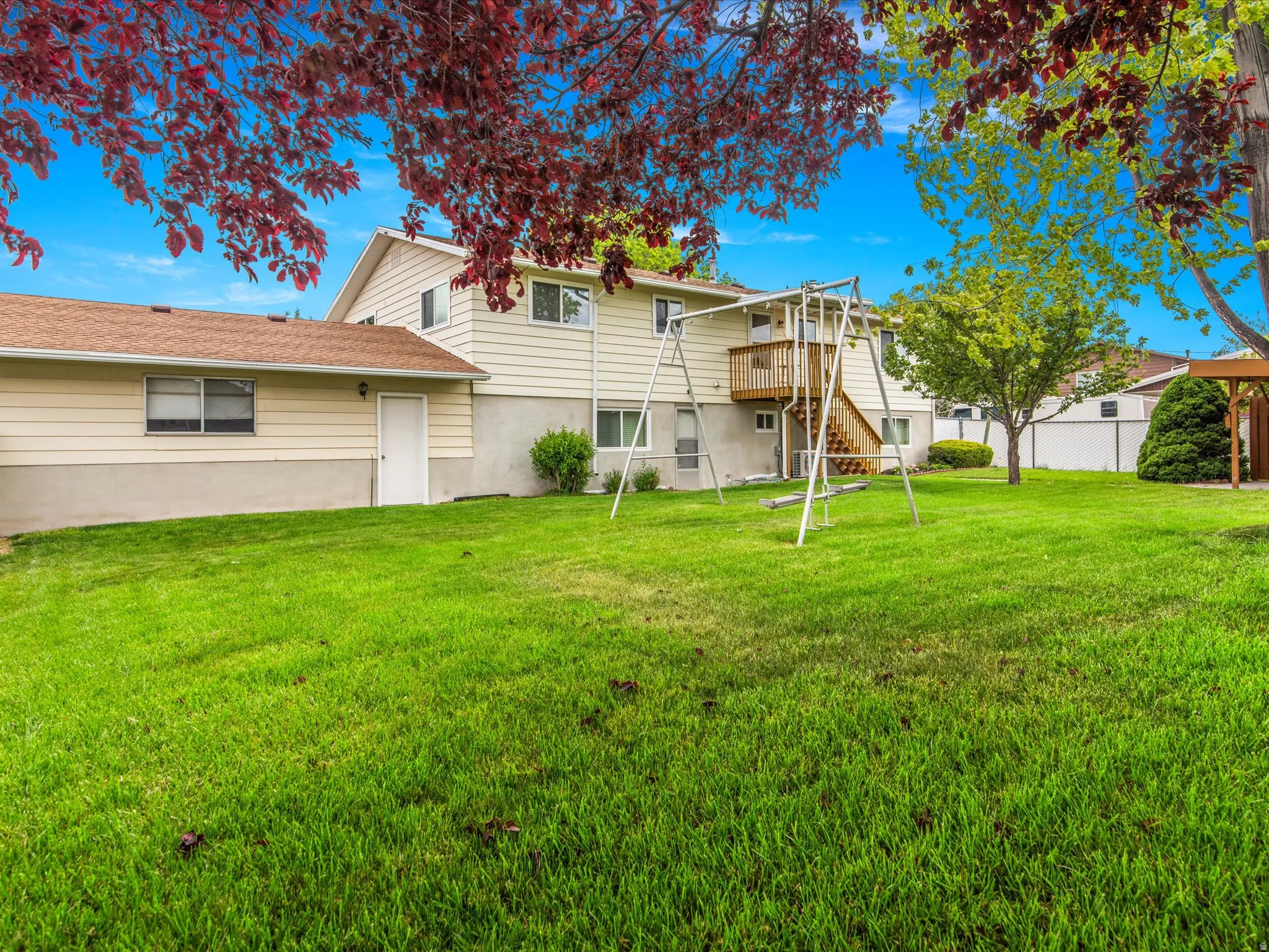 Expansive green lawn with mature trees and a private rear deck featuring exterior stairs