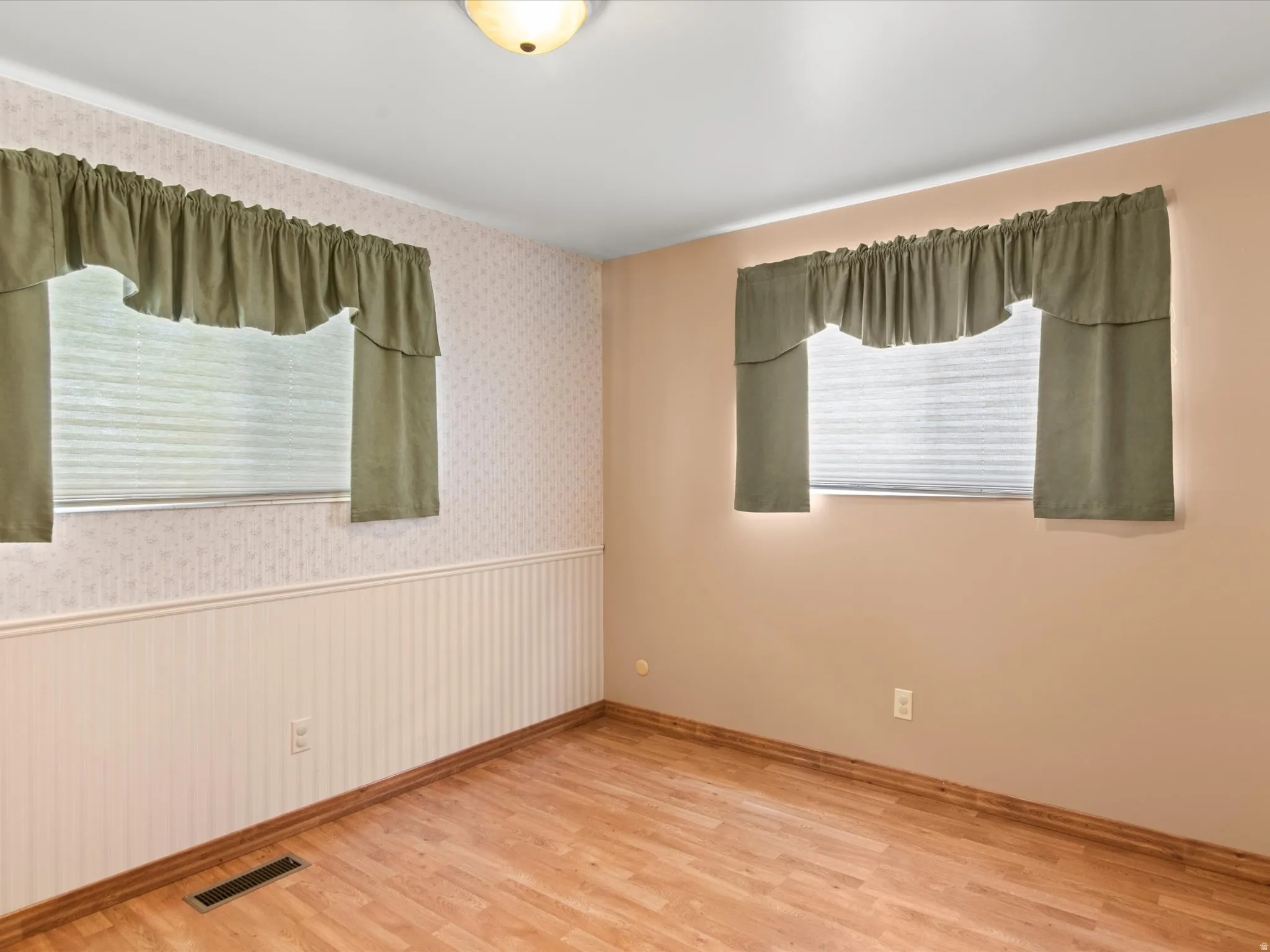 Room featuring wood-finish flooring, two windows with blinds, and a ceiling-mounted light fixture