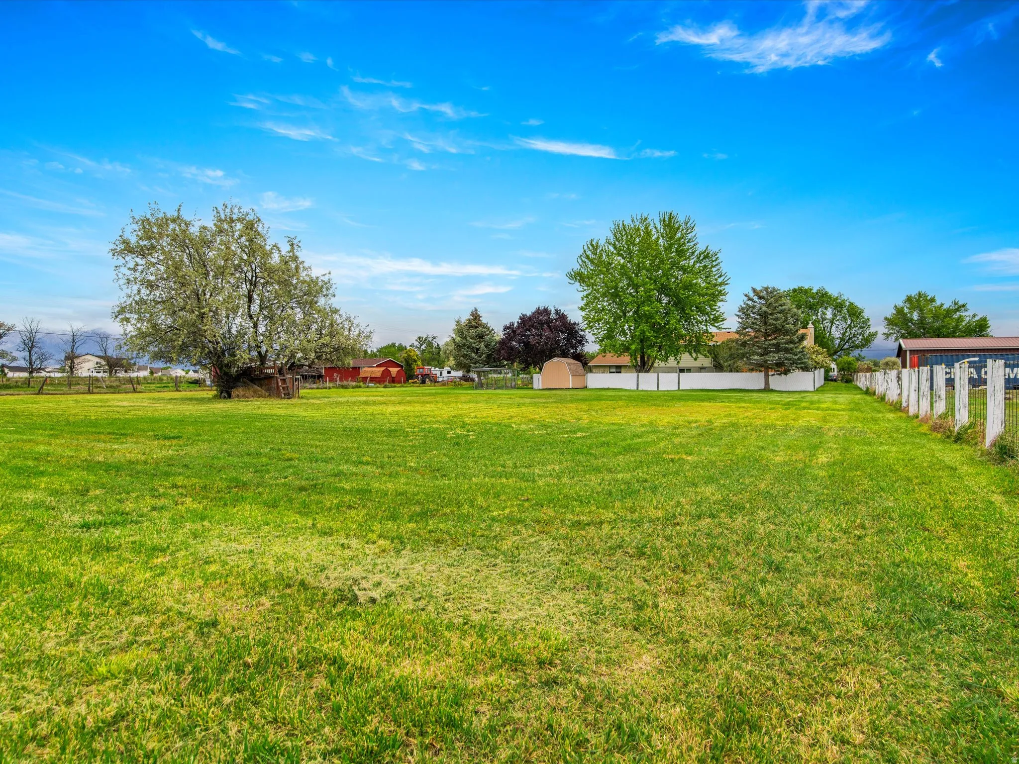 Expansive green lawn with a white post fence and mature trees